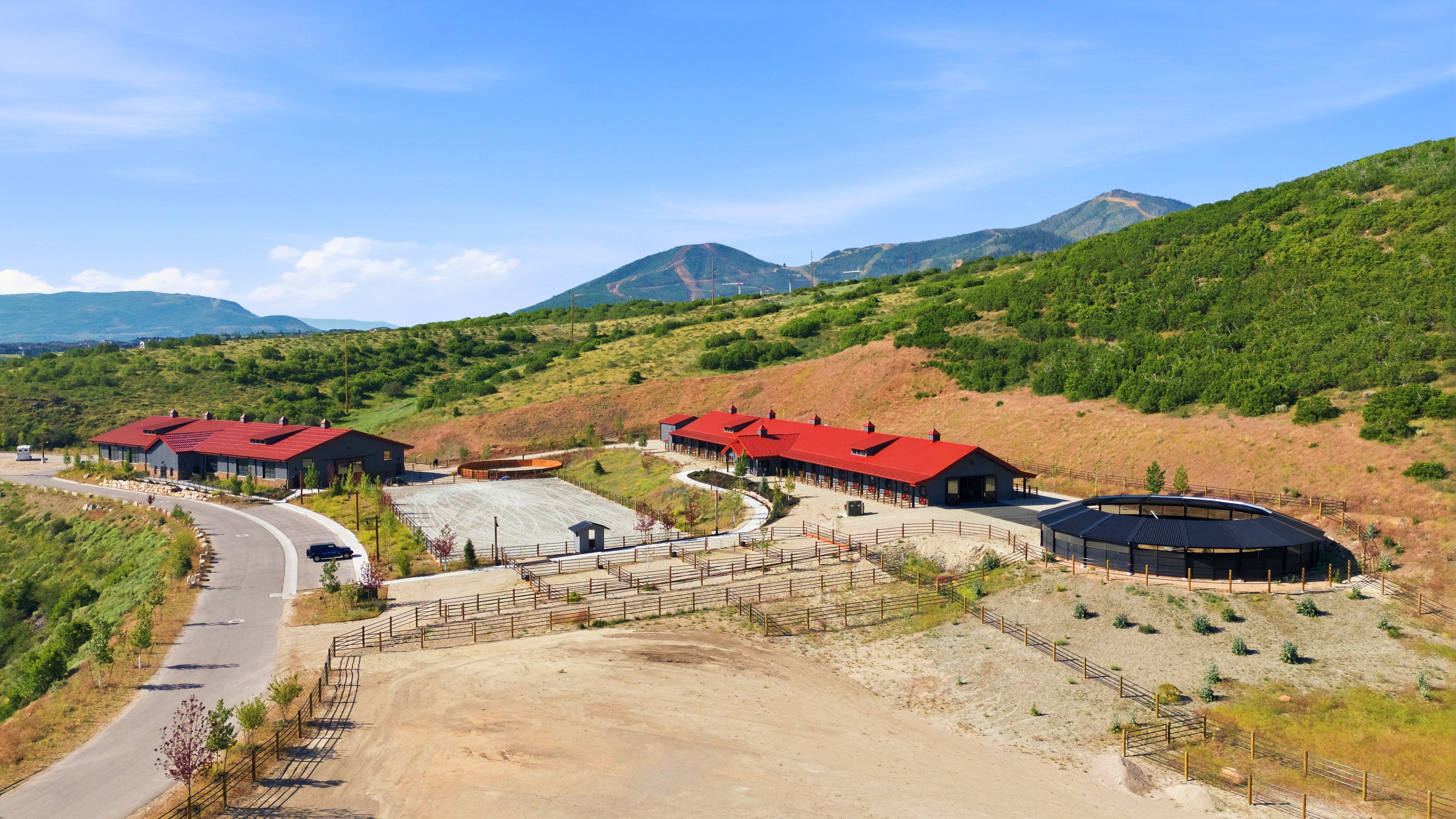 Extensive equestrian facility featuring multiple buildings with red roofs, a circular riding arena, and a large paved parking area