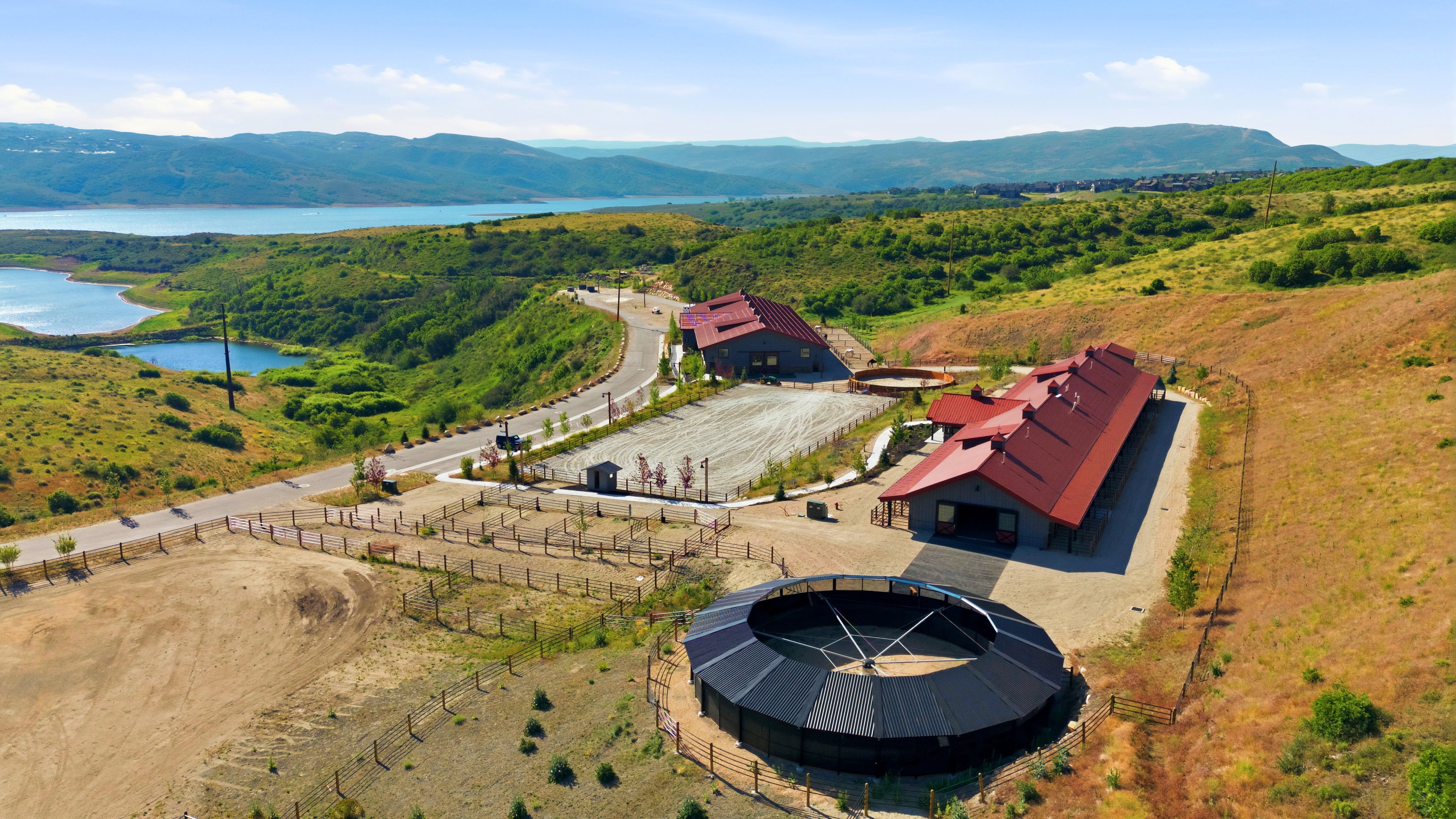 Aerial depiction of a property featuring two structures with red roofs, a large circular arena, and surrounding open land