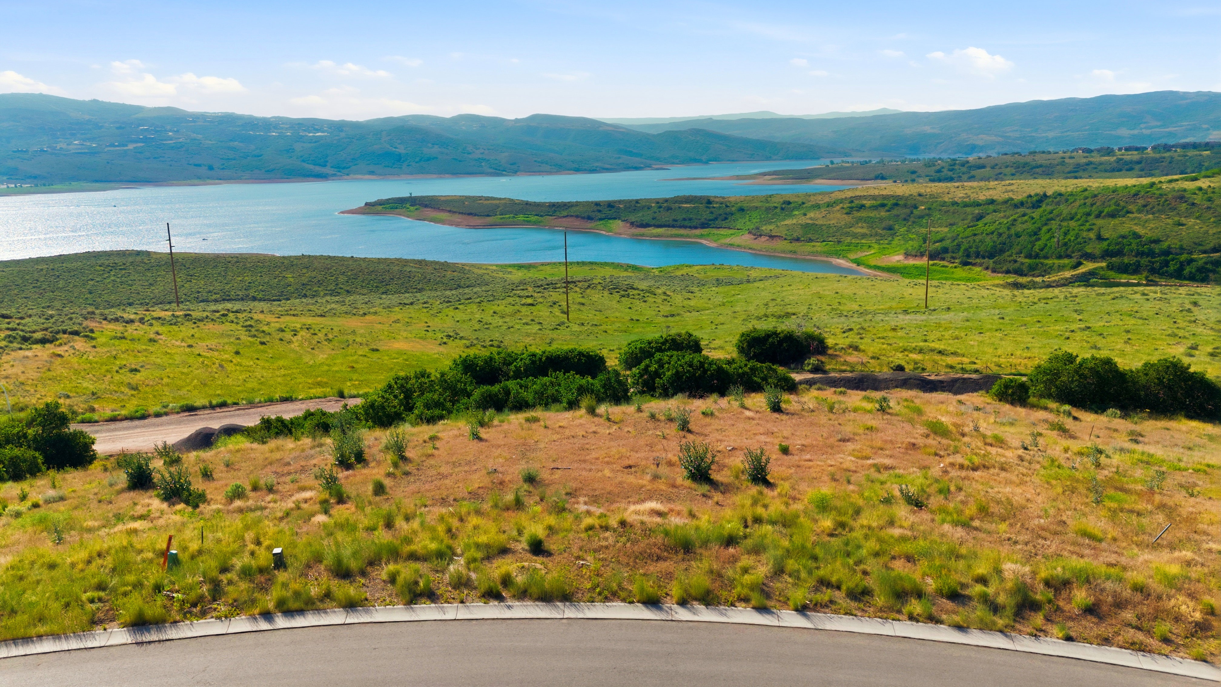 Expansive parcel featuring a paved road frontage, natural landscaping, distant water body, and rolling hills
