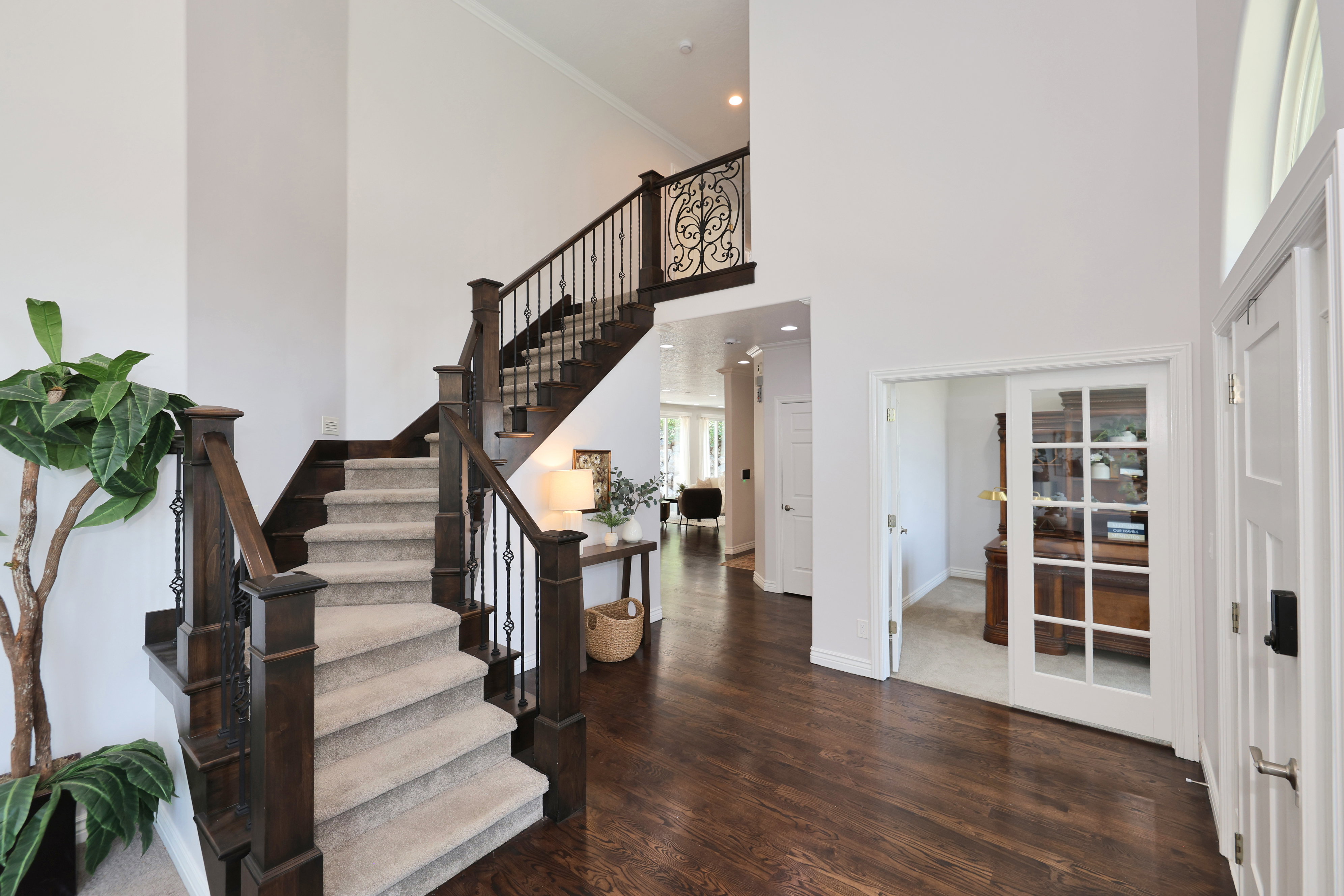 Two-story foyer featuring dark wood-finish flooring, a grand staircase with carpeted treads, dark wood newel posts, and wrought iron balusters, and a doorway with French doors
