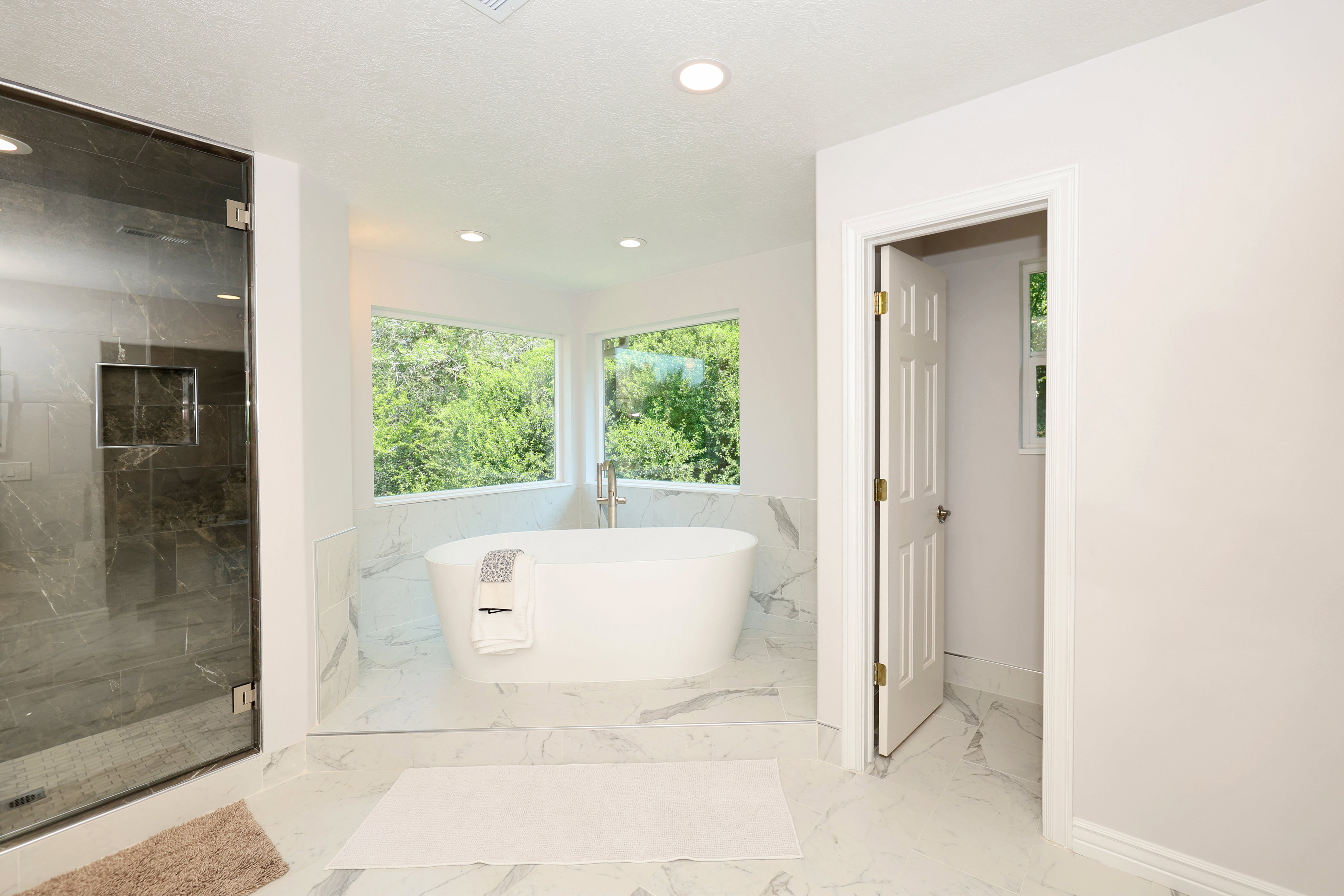 Freestanding soaking tub with floor-mounted faucet set on a tiled platform, surrounded by expansive windows