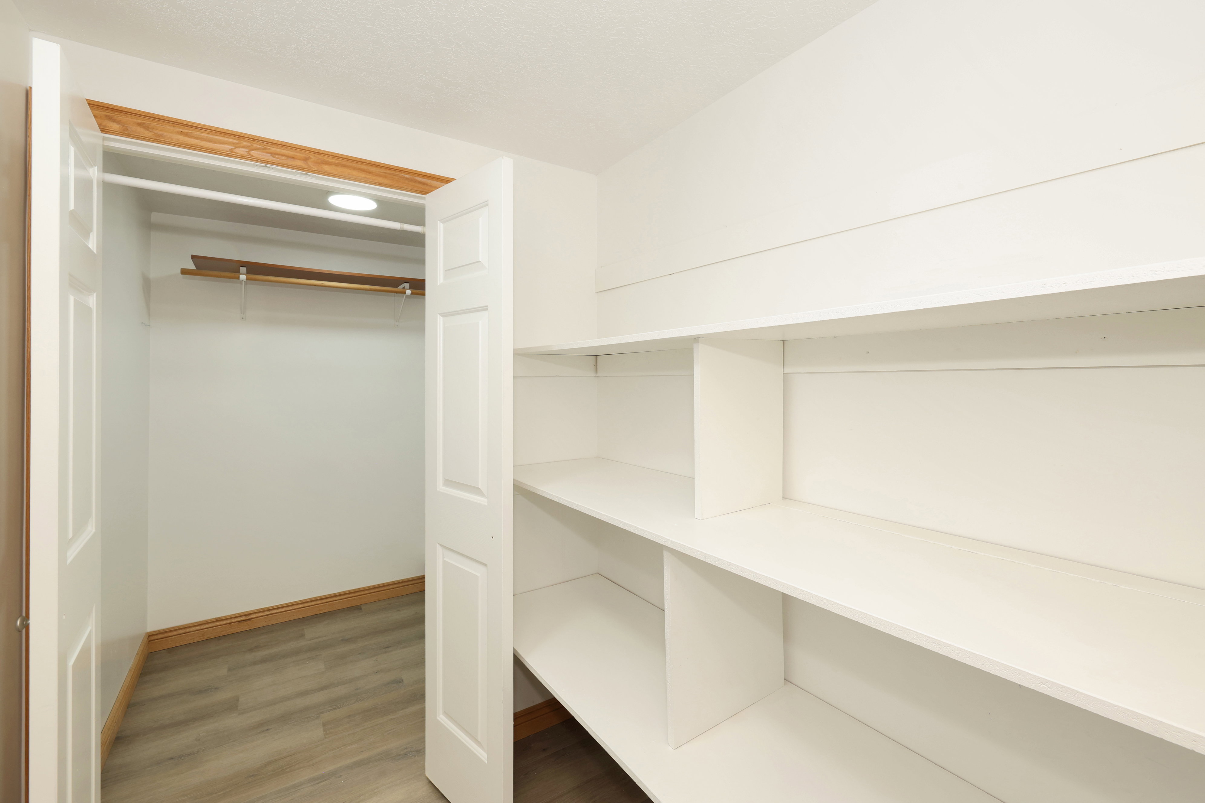 Bright white pantry and storage area featuring built-in shelving, wood-finish flooring, and a recessed ceiling light