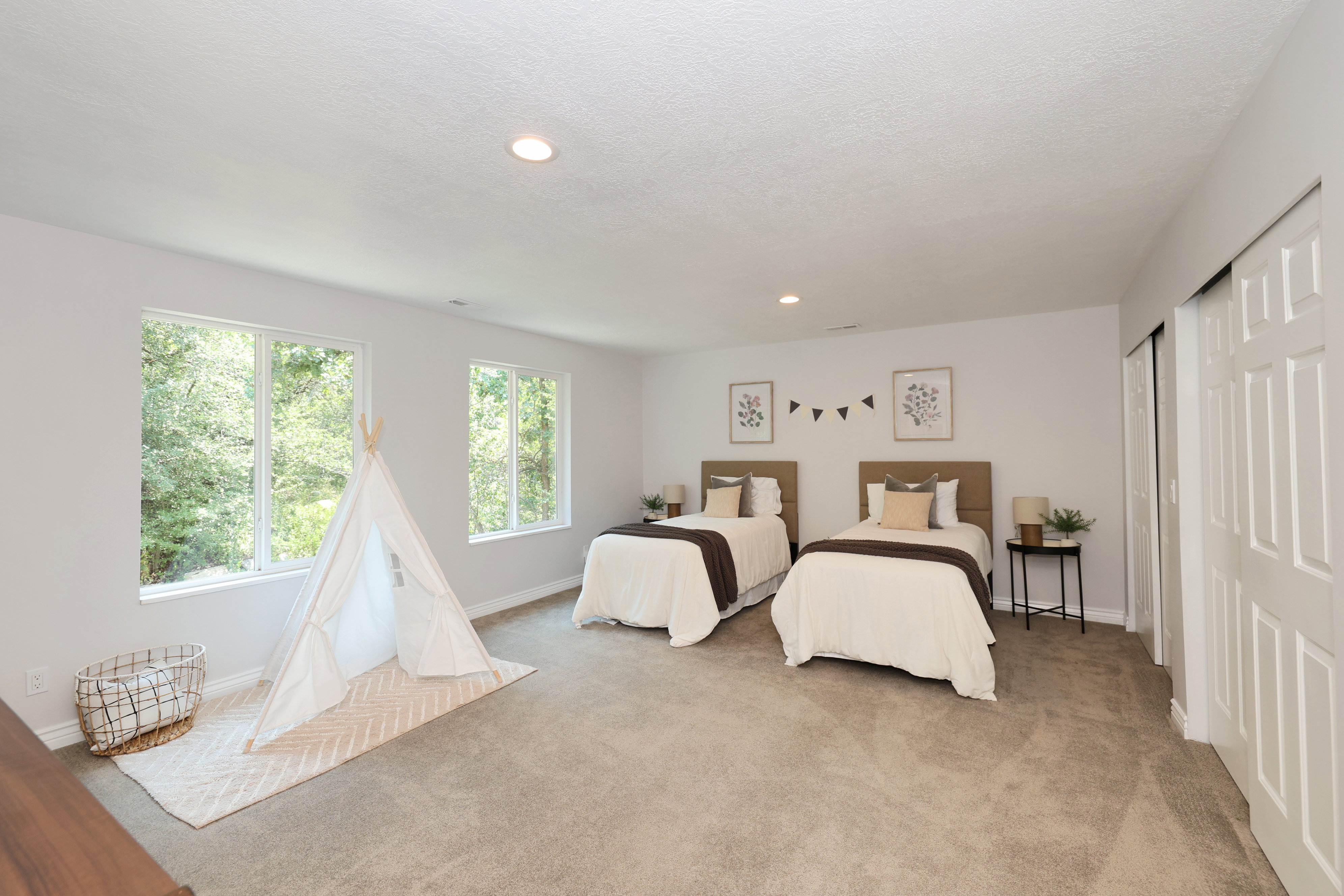 Spacious room featuring light gray wall paint and two large windows offering verdant exterior views