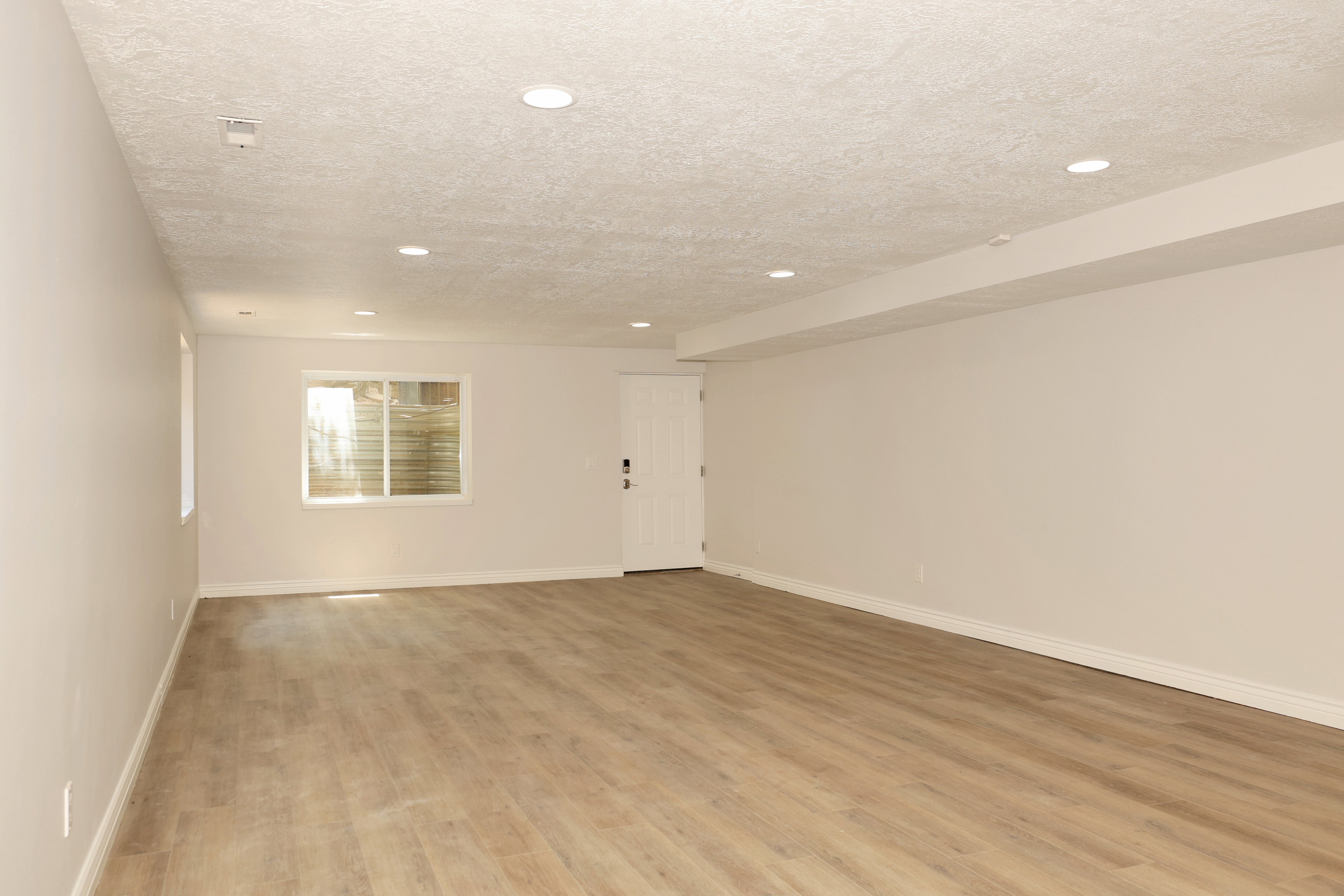 Spacious room with wood-finish flooring, recessed lighting, white walls, and a visible window well