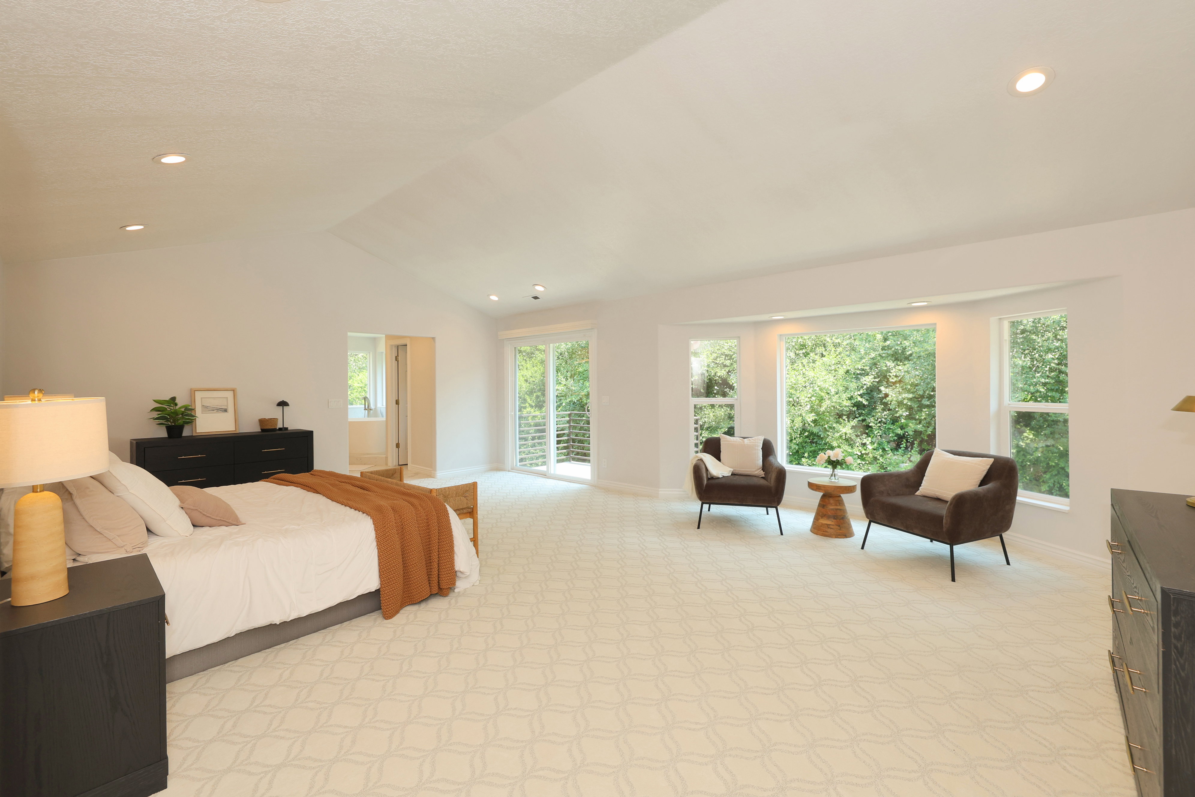 Expansive room featuring vaulted ceilings, recessed lighting, patterned carpeting, a large bay window, and sliding glass doors to a balcony