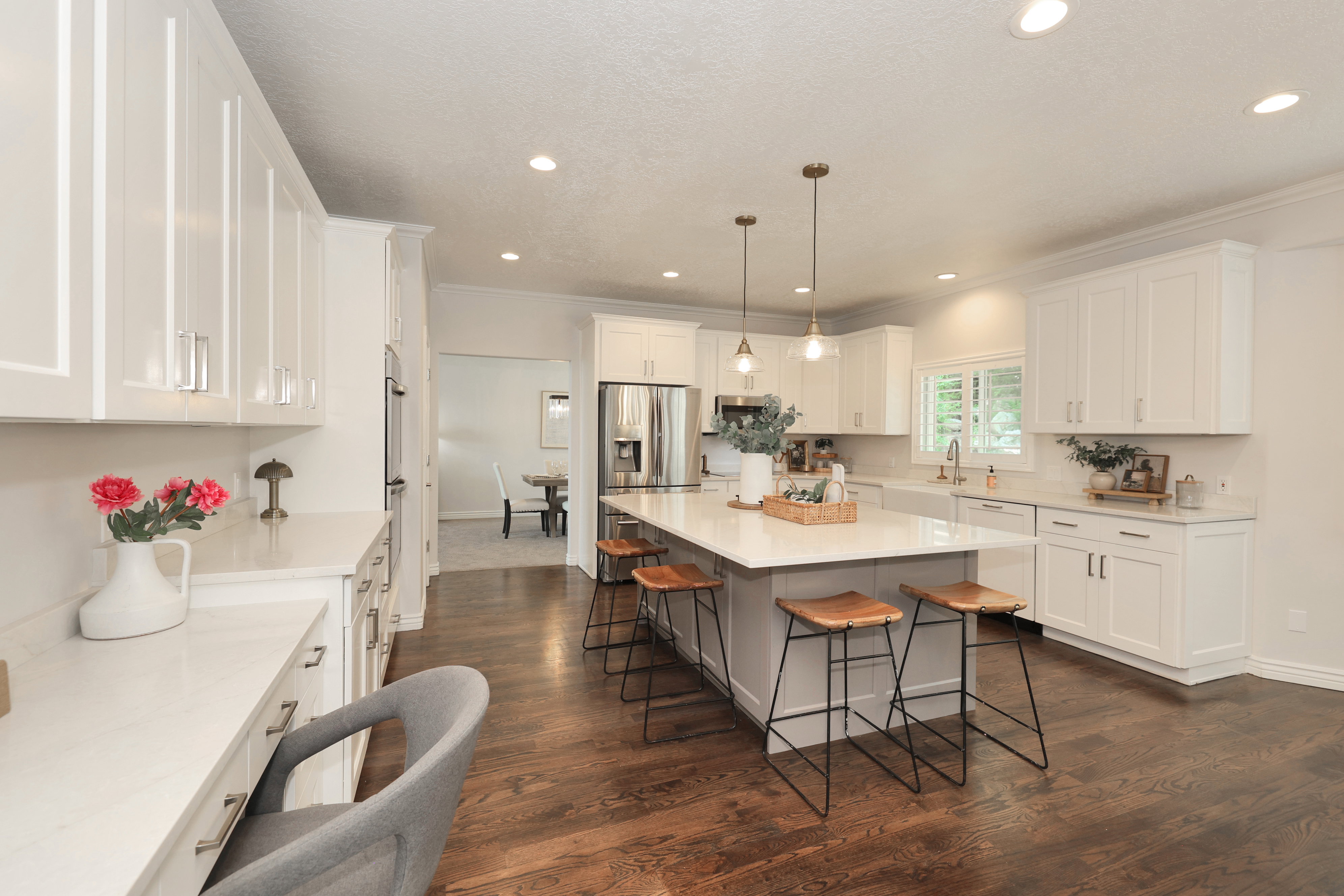 Spacious kitchen featuring an expansive center island with pendant lighting, white shaker cabinetry, stainless steel appliances, white countertops, and wood-finish flooring