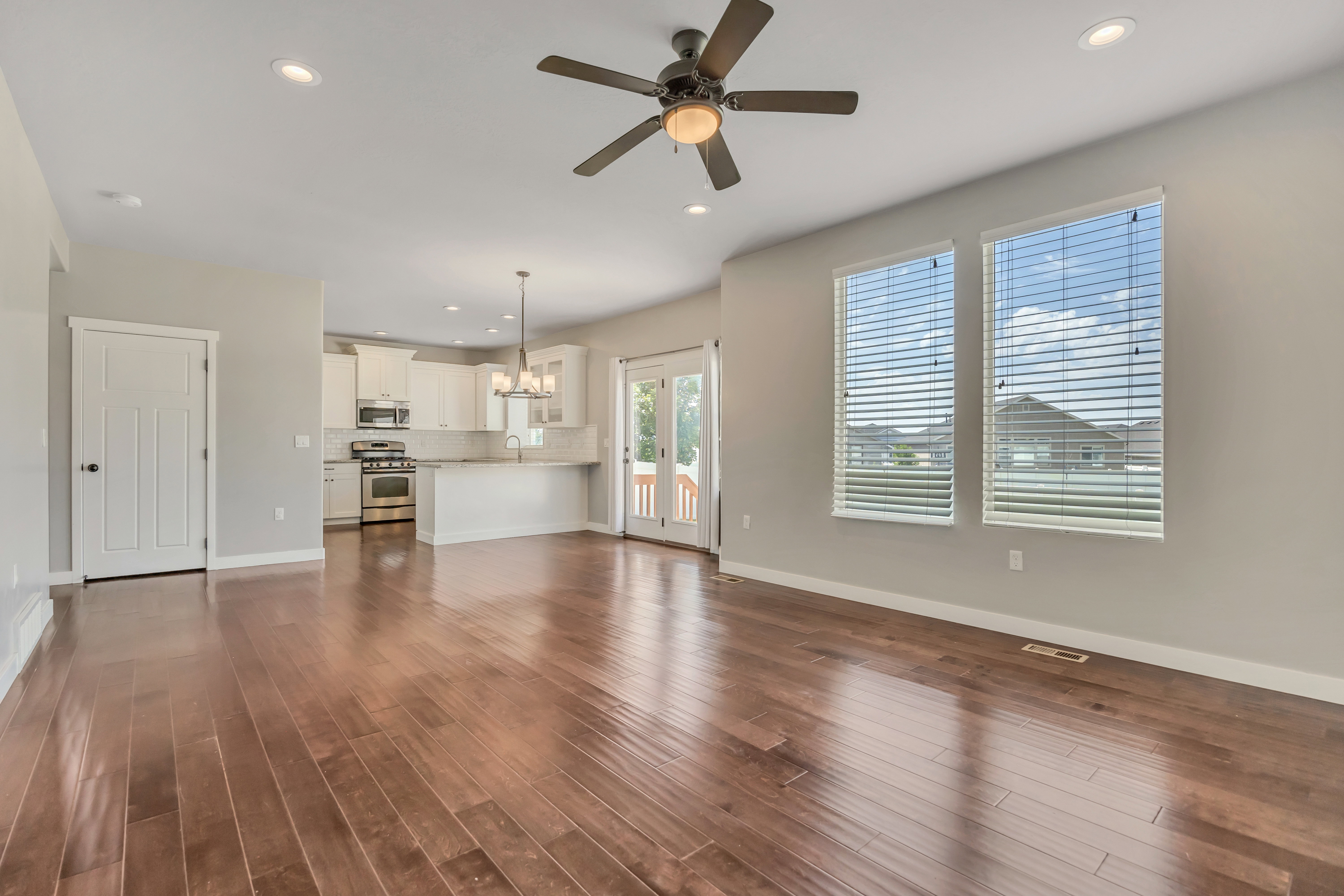 Expansive open-concept living area featuring wood-finish flooring, two large windows with blinds, and recessed lighting