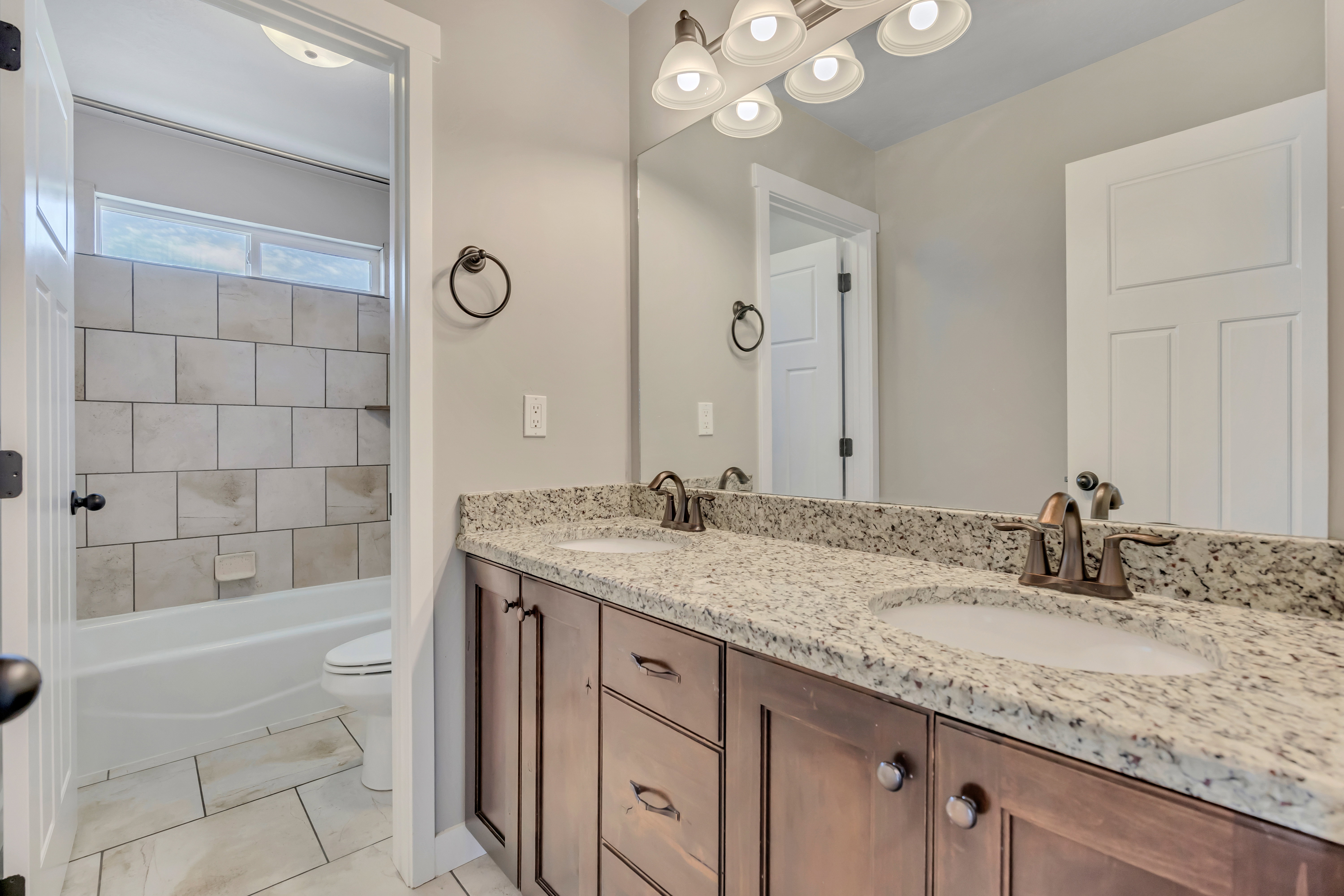 Bathroom featuring a double vanity with stone countertops, a large mirror, and a five-light fixture