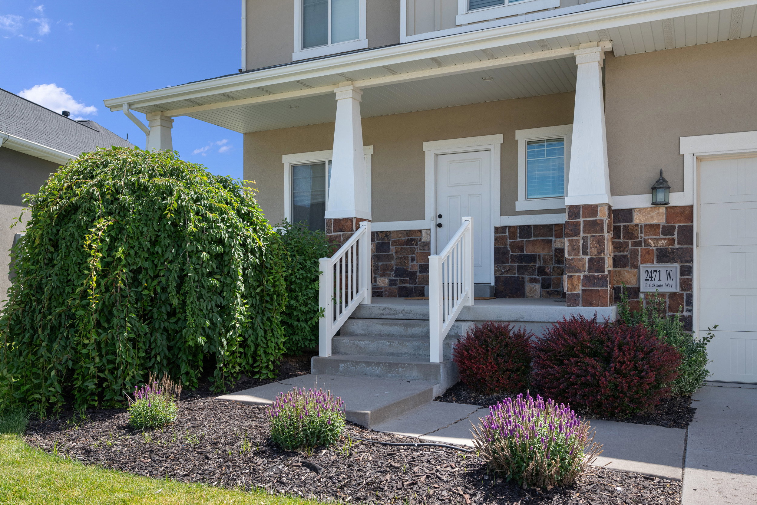 Covered front porch with stone accents, concrete steps, and white railing