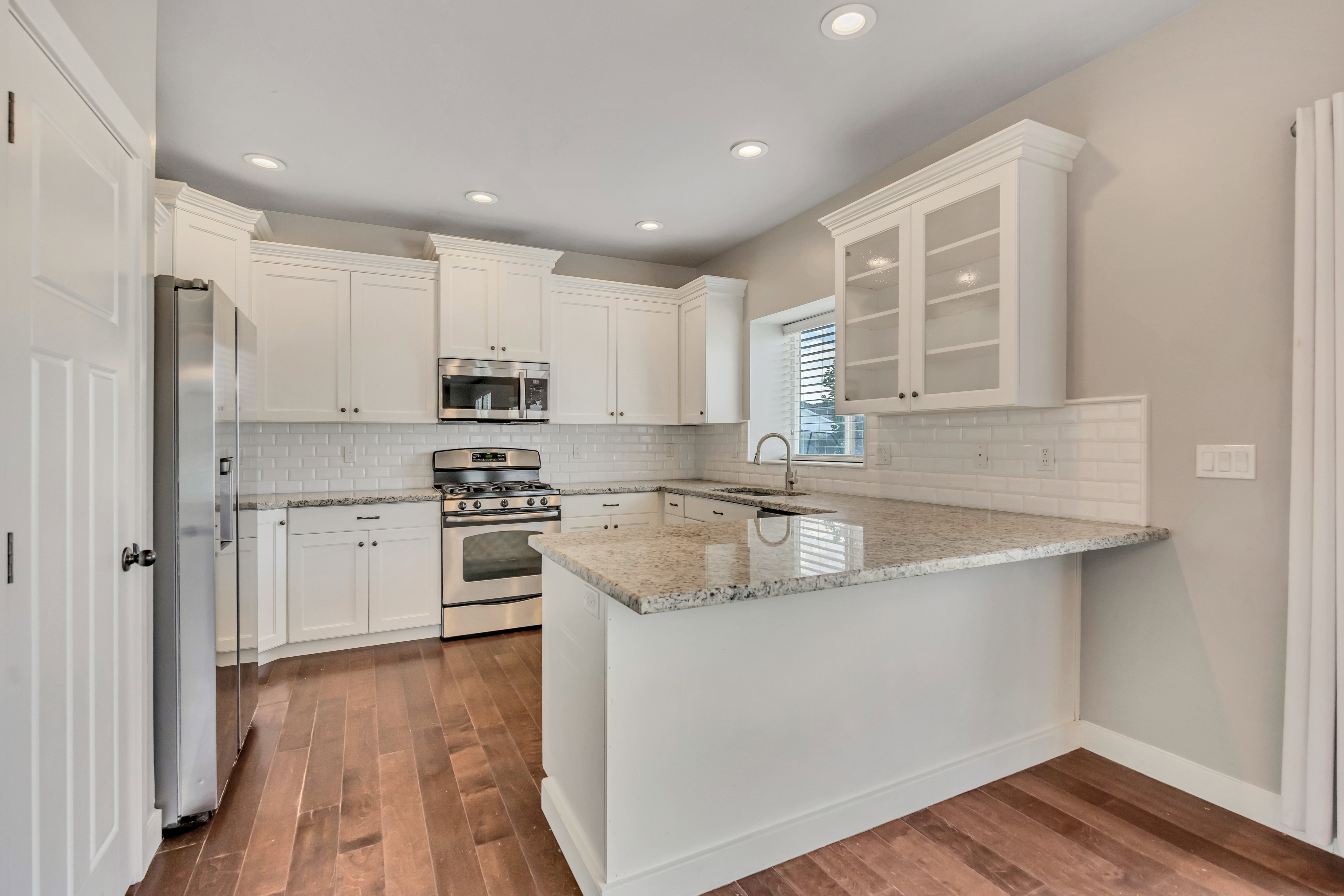 Kitchen featuring white cabinetry, stainless steel appliances, granite countertops, subway tile backsplash, and wood-finish flooring
