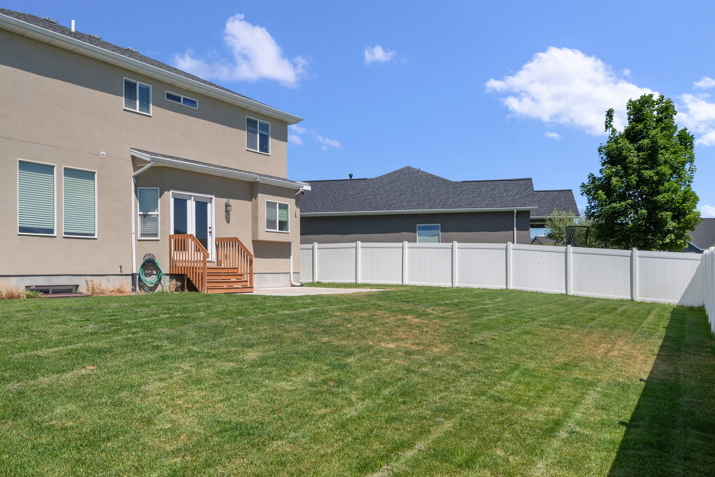 Expansive rear yard featuring a manicured lawn, full vinyl privacy fencing, and a wooden deck with stairs providing outdoor access