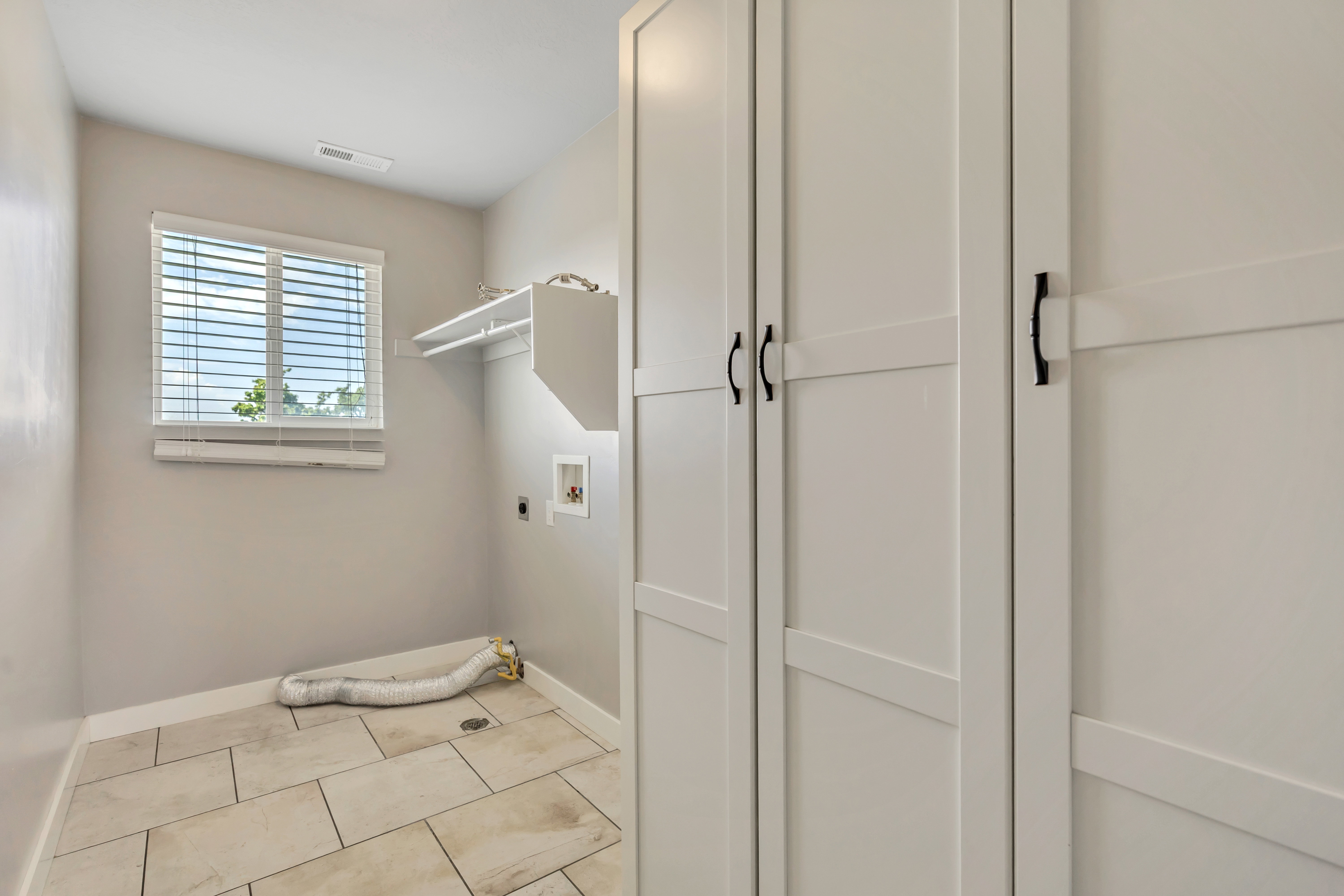Laundry area featuring neutral wall paint, tile flooring, a window with blinds, and built-in white cabinetry with matte black hardware