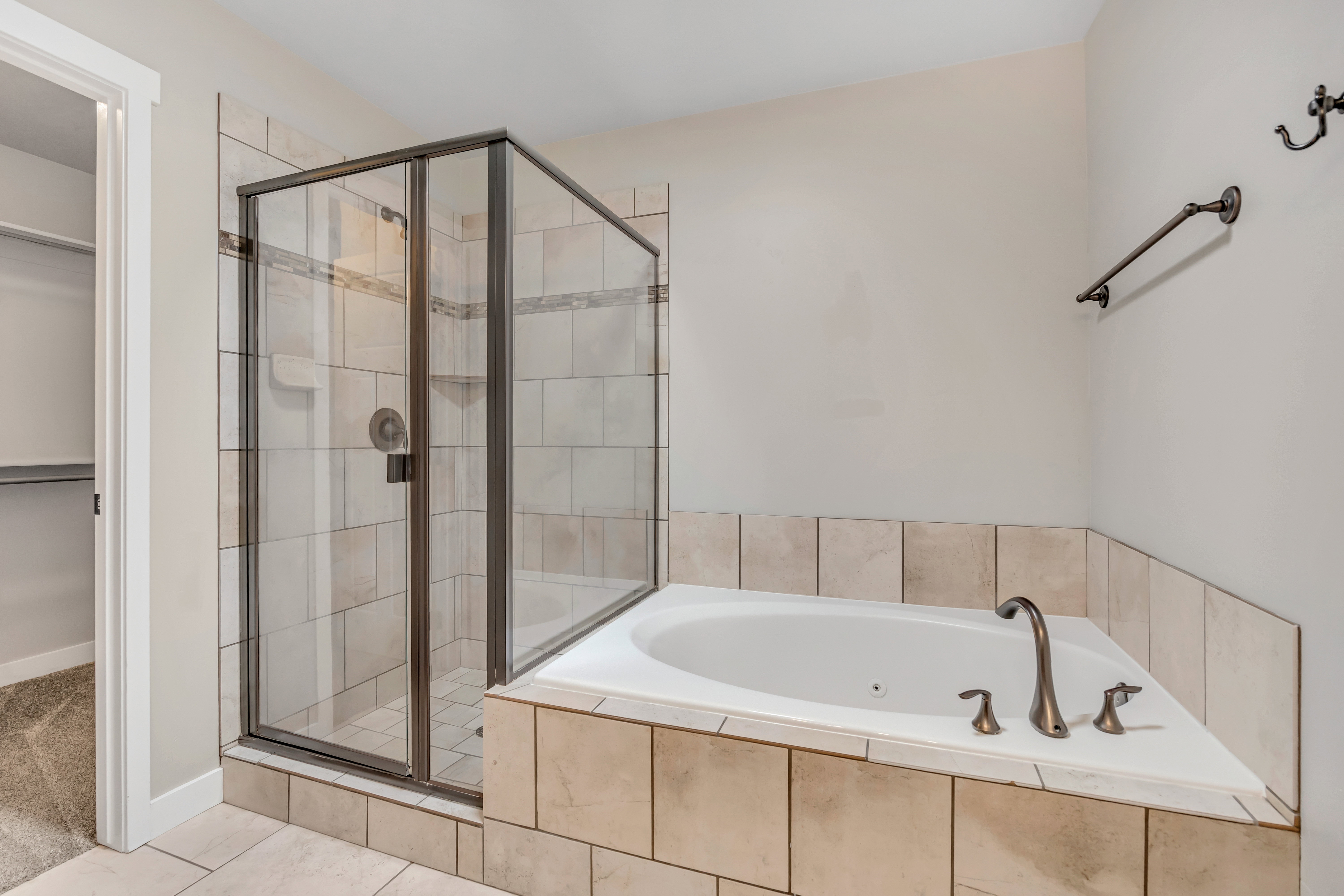 Corner soaking tub with bronze-finish fixtures, tile surround, and an adjacent glass-enclosed shower with tile walls