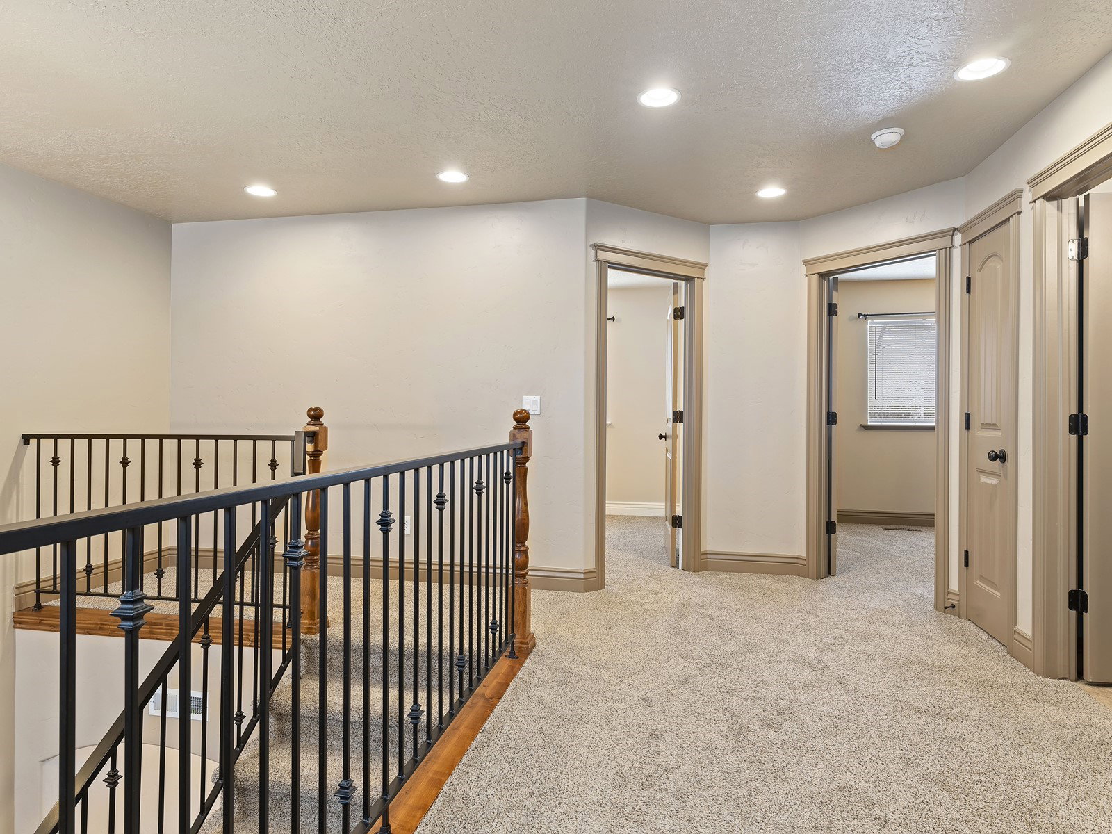 Upper-level hallway featuring plush carpeting, recessed lighting, and a wrought iron and wood banister