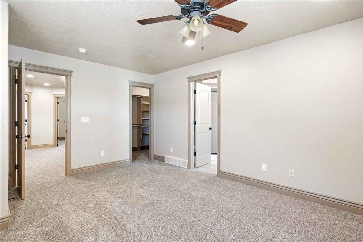 Spacious room featuring light gray walls, plush carpet flooring, and a ceiling fan with light fixture