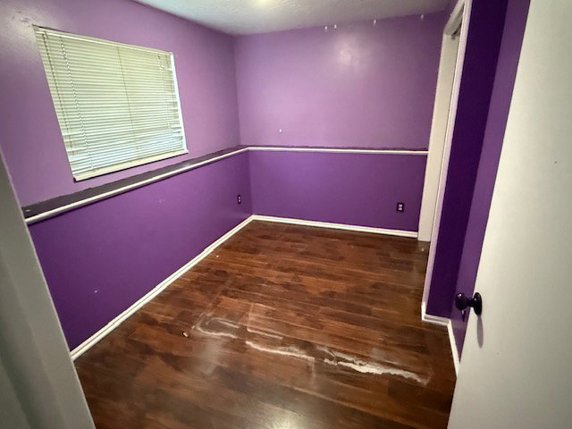 Room with wood-finish flooring, a window featuring horizontal blinds, and a white trim baseboard
