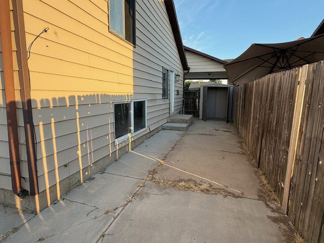 Concrete pathway alongside the home, featuring a wood fence, exterior siding, and a storage shed