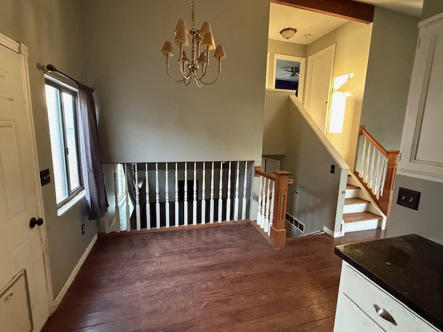 Split-level interior featuring wood-finish flooring, a traditional chandelier, multiple windows, and a staircase with wood newel posts and white balusters
