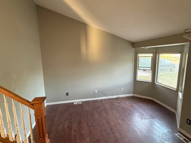 Spacious room featuring wood-finish flooring, a bay window, and a vaulted ceiling