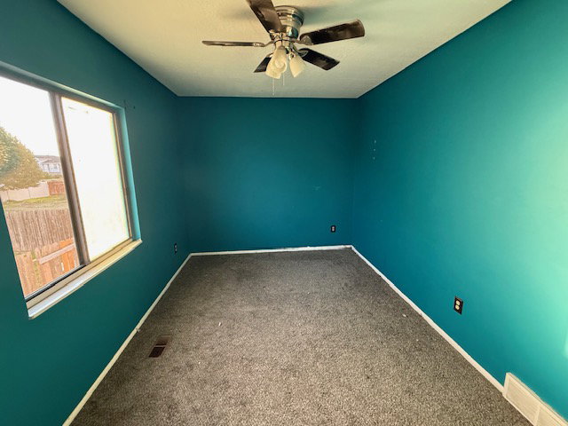 Room featuring teal walls, gray carpet, and a ceiling fan