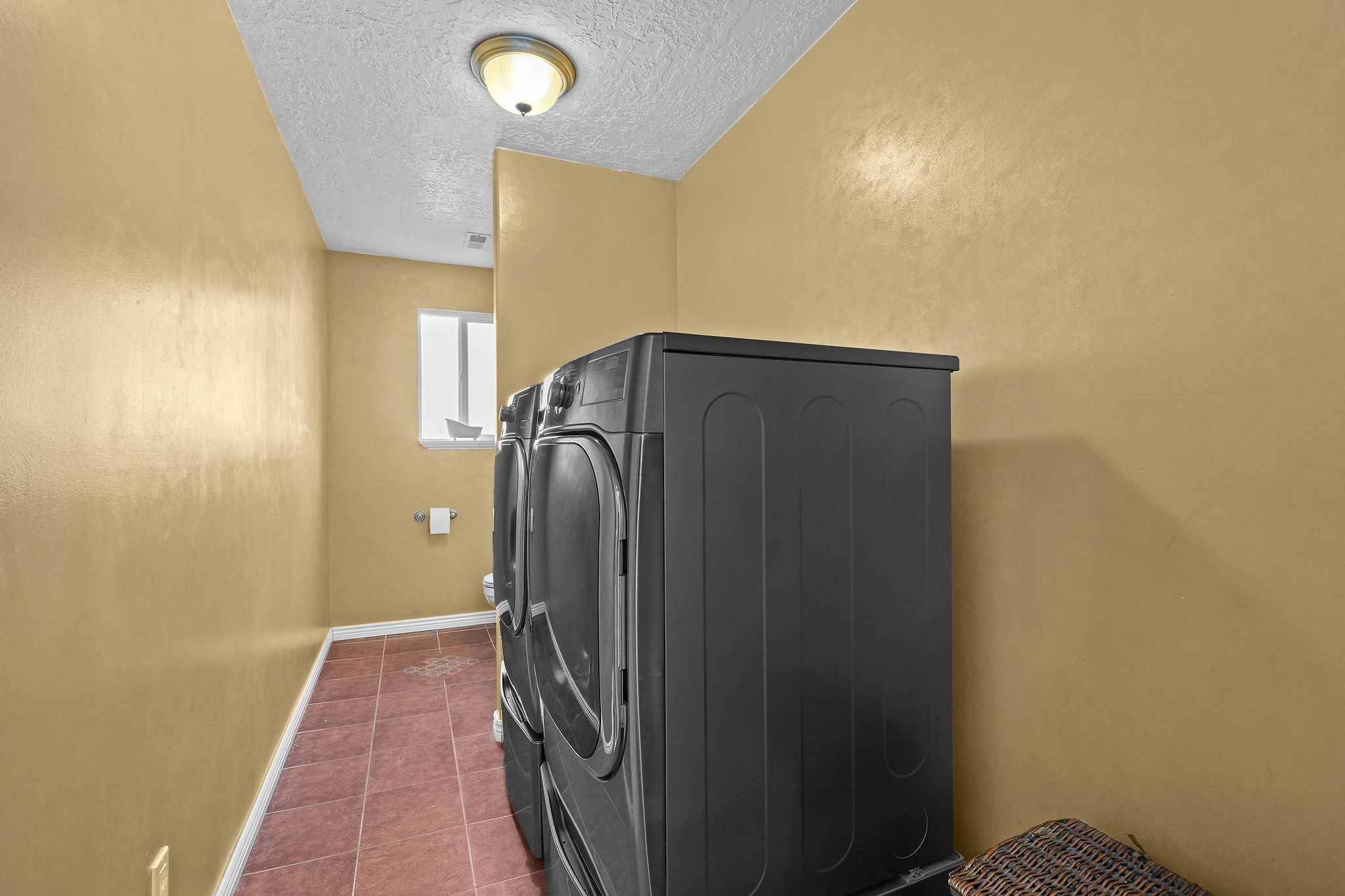 Dedicated laundry area with warm-toned walls, tile flooring, and a ceiling-mounted light fixture