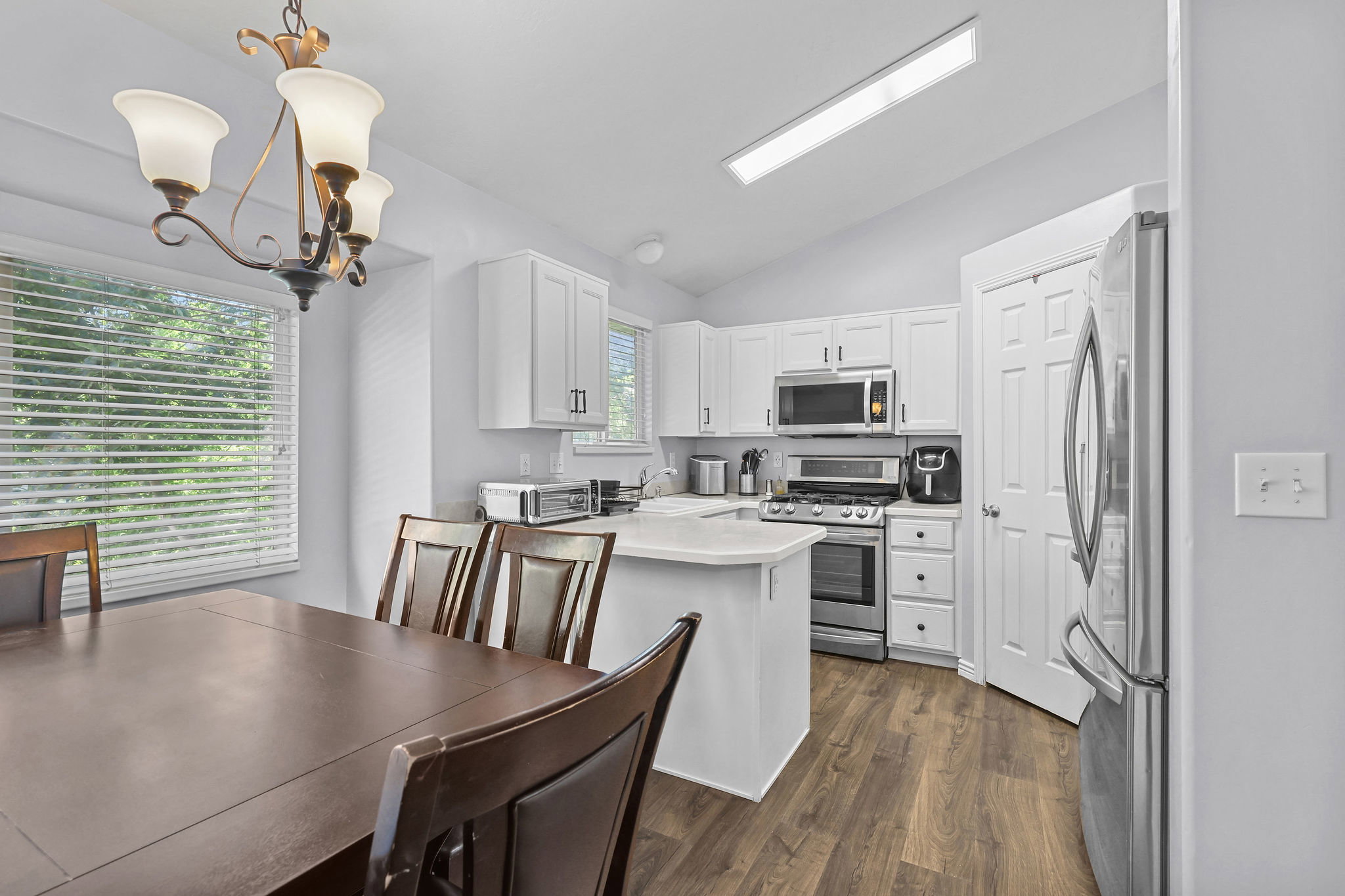 Kitchen and dining area featuring wood-finish flooring, white cabinetry, stainless steel appliances, and a vaulted ceiling