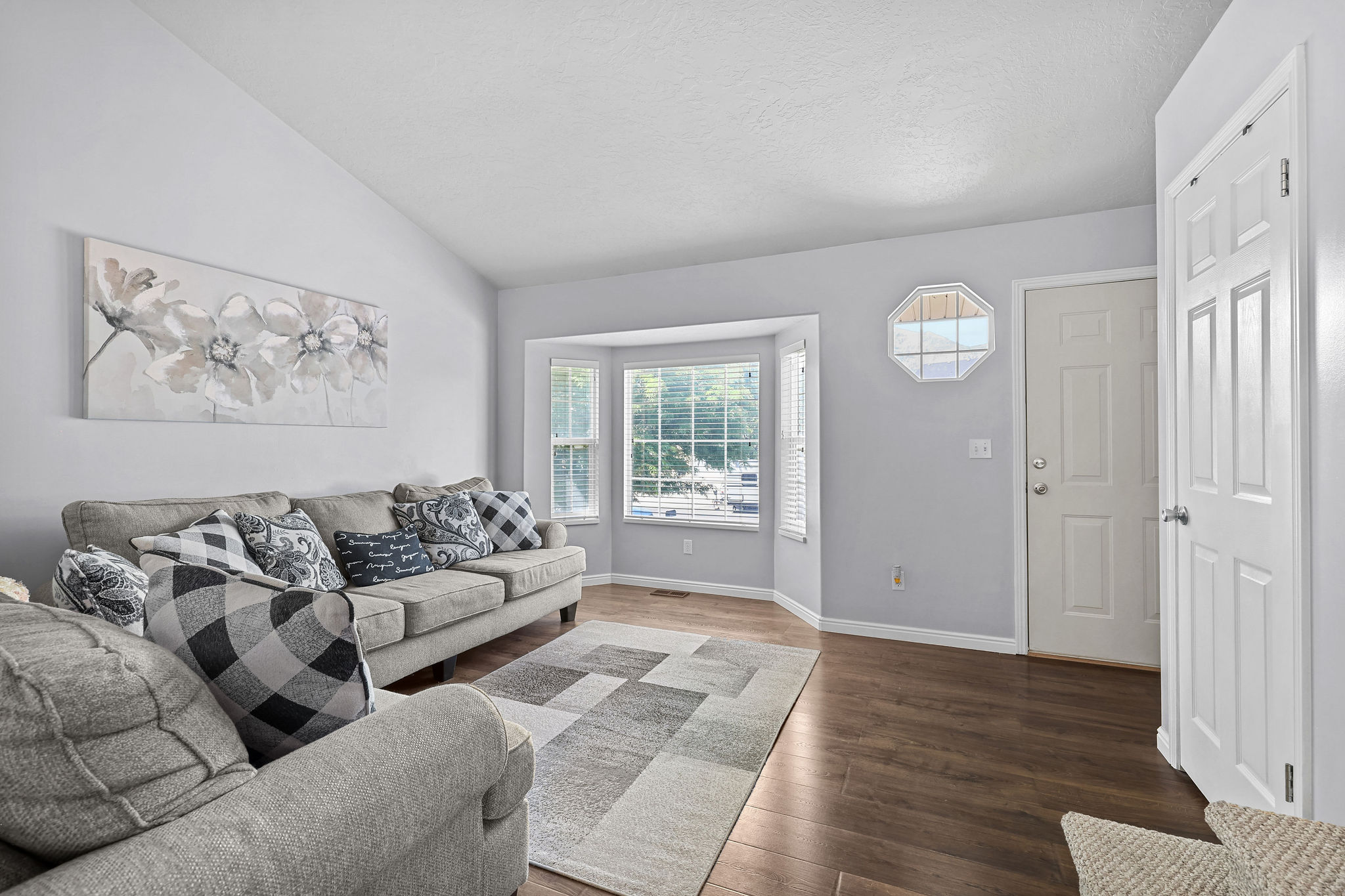 Living area featuring wood-finish flooring, a bay window with multiple panes, and a vaulted ceiling