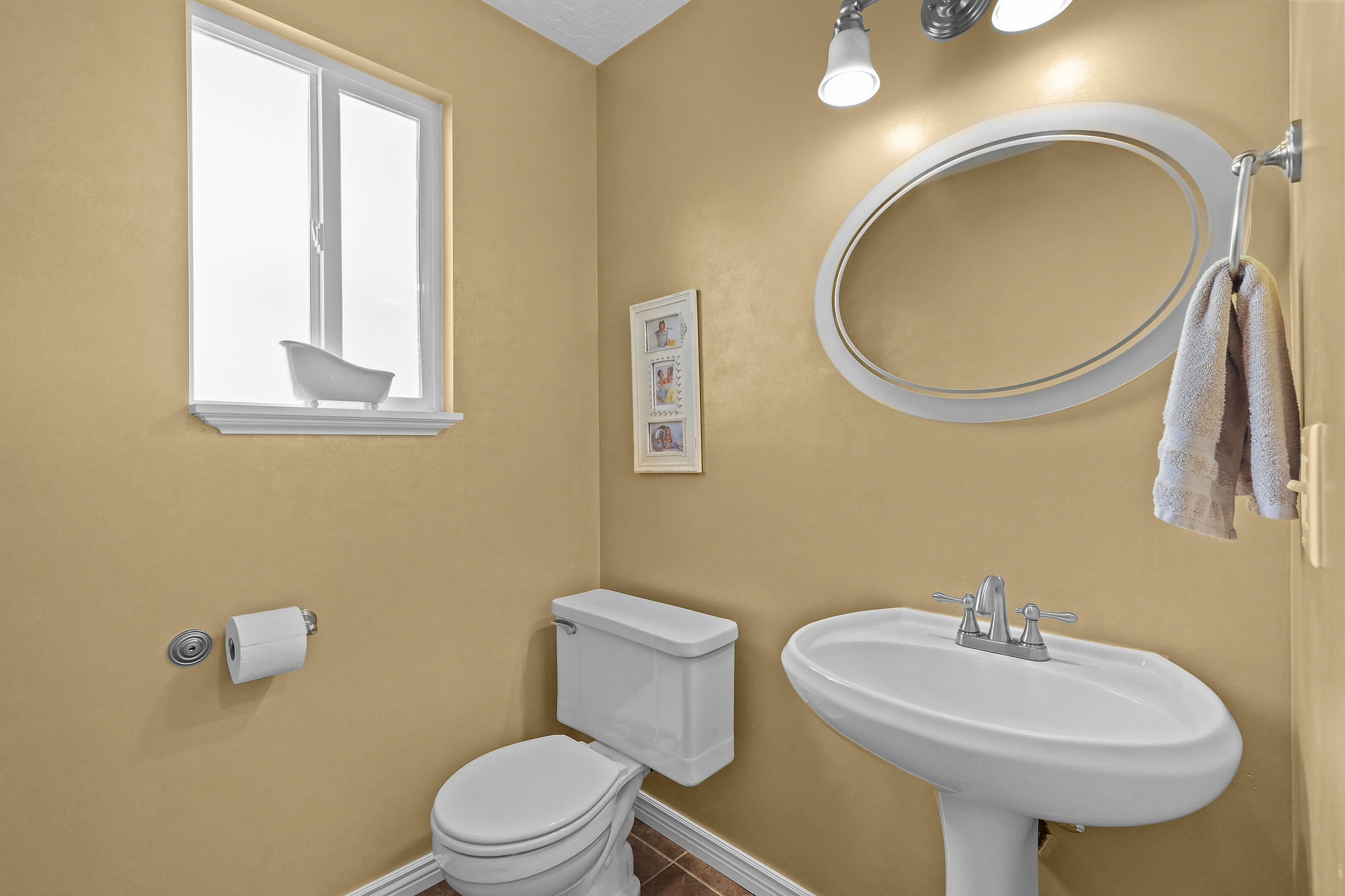 Pedestal sink with chrome faucet, oval mirror, and overhead lighting fixture