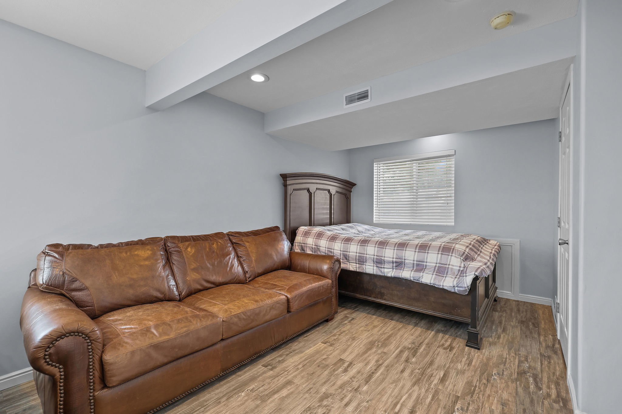 Recessed lighting illuminates this versatile space featuring wood-finish flooring, a window with blinds, and light gray walls