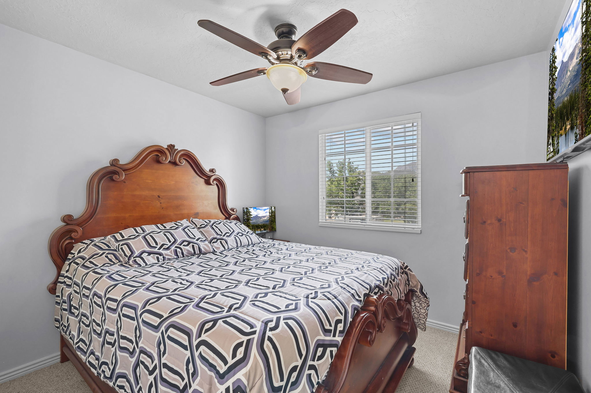 Bedroom featuring a ceiling fan with integrated lighting, a single window with horizontal blinds, neutral wall paint, and textured carpet flooring