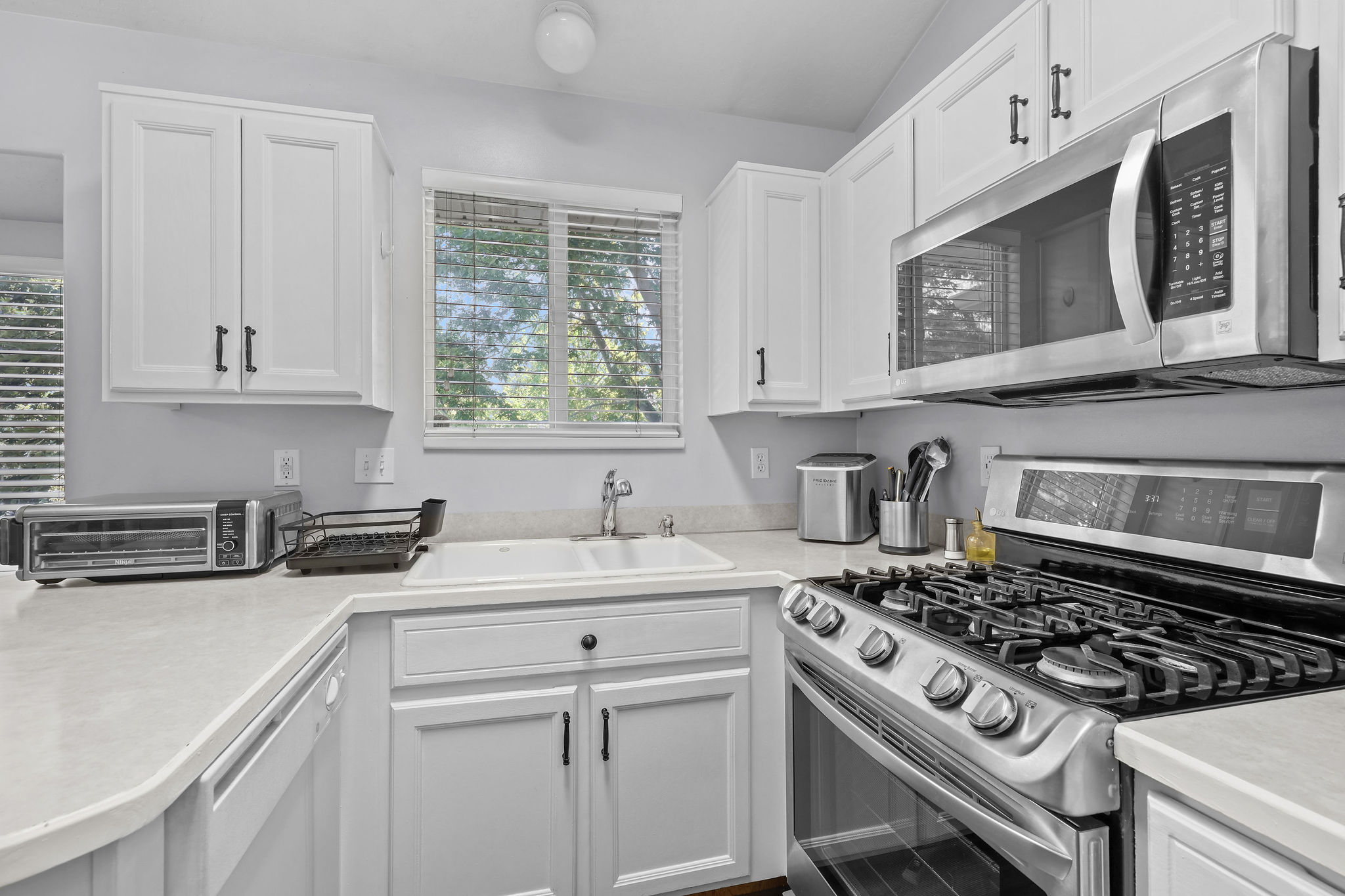Kitchen featuring white cabinetry with dark hardware, stainless steel gas range, stainless steel microwave, light-toned countertops, and a white sink
