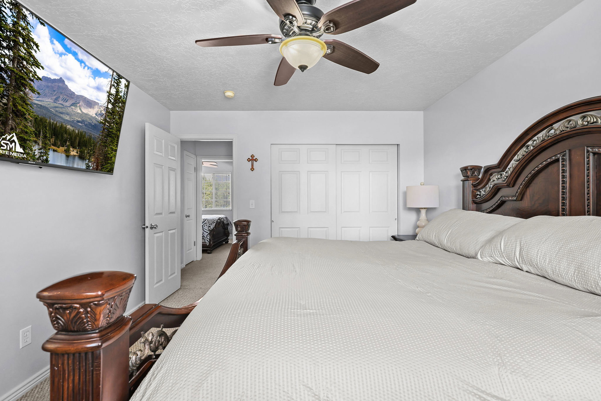 Spacious bedroom featuring light-toned walls, a ceiling fan with integrated lighting, and a large wall-mounted screen