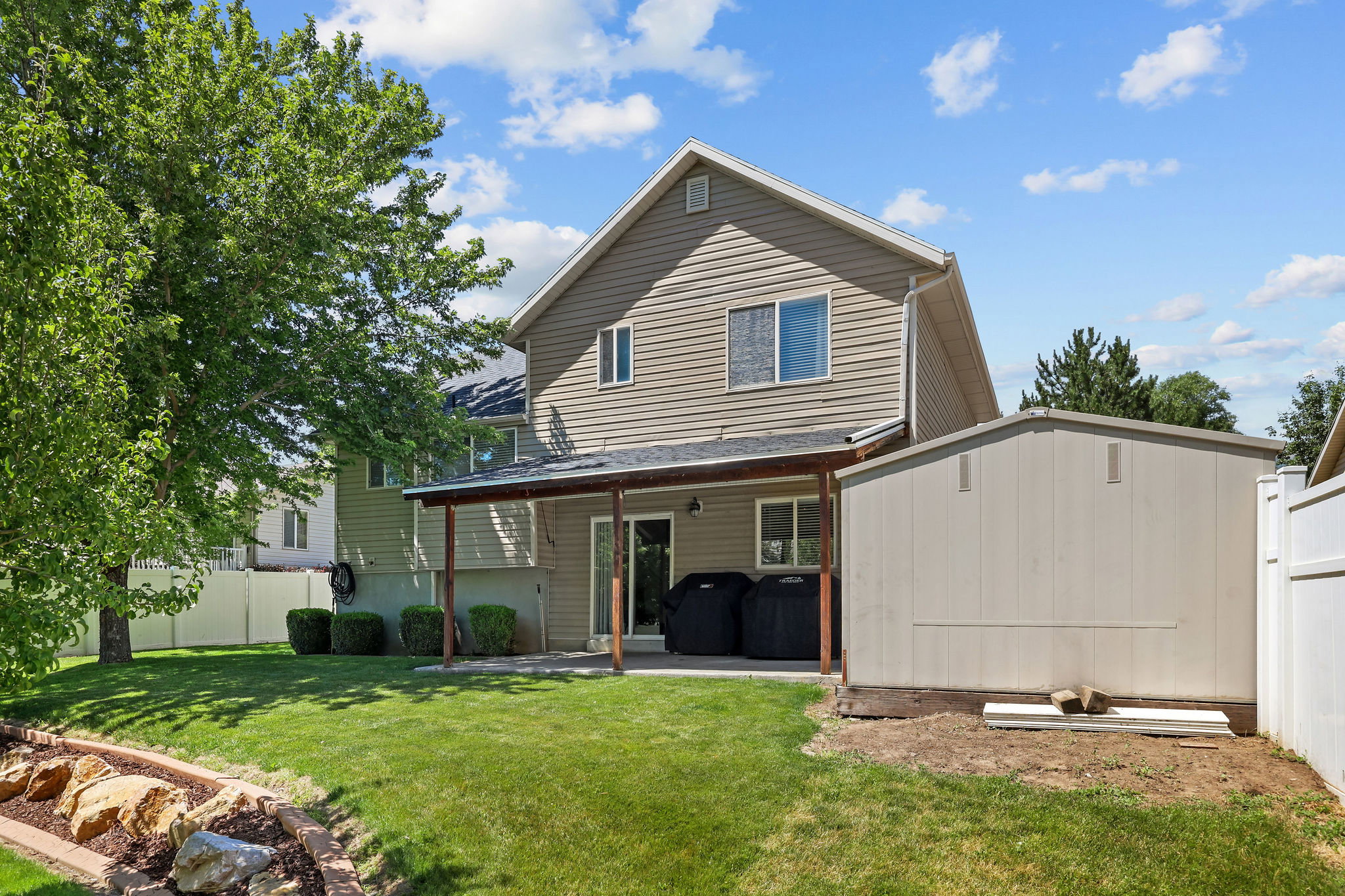 Expansive backyard with a manicured lawn, established landscaping, and a covered patio