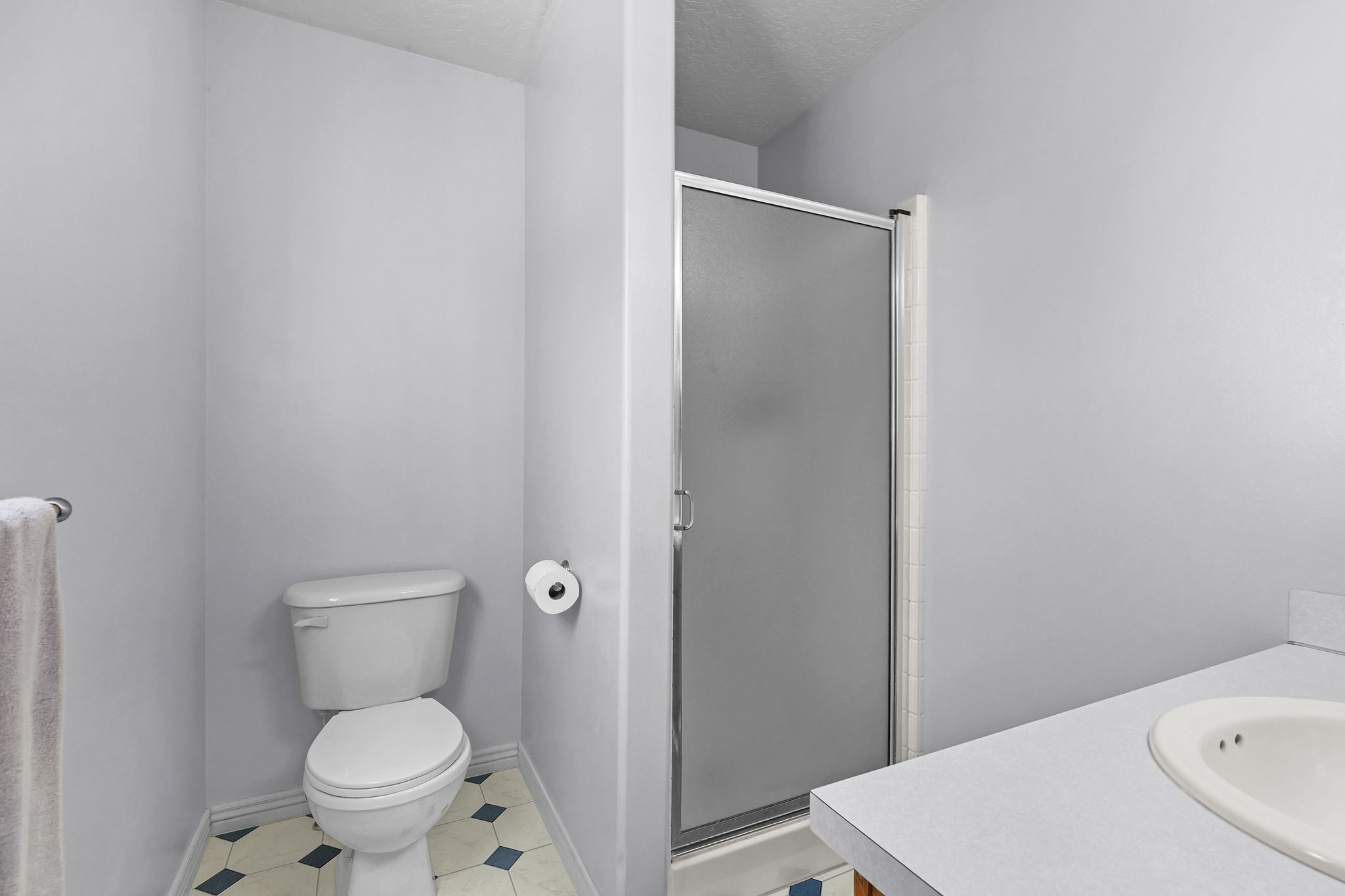 Bathroom featuring a white toilet, enclosed shower with frosted glass, built-in vanity with integrated sink, and patterned floor tiling