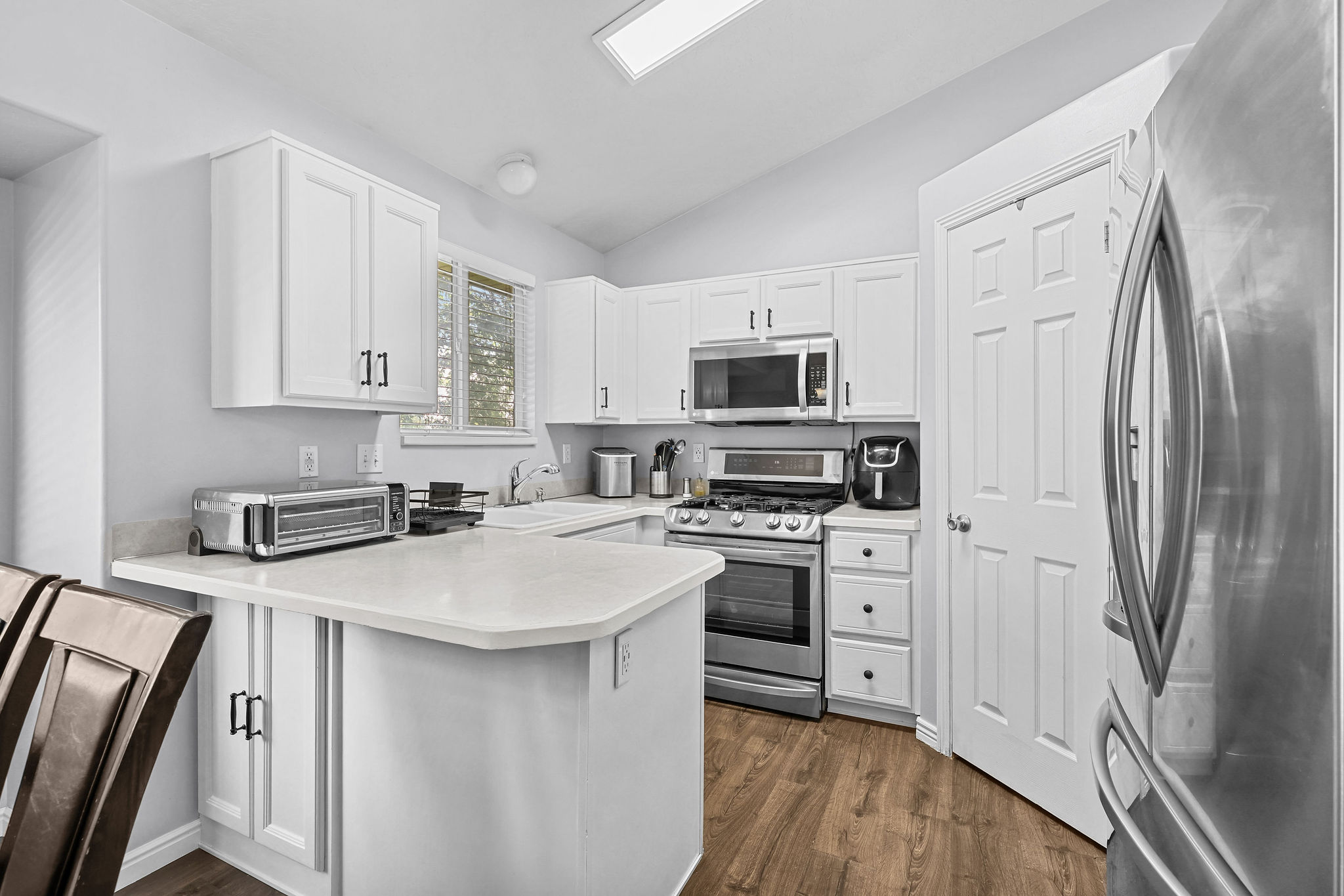 Kitchen featuring white shaker cabinetry with dark hardware, stainless steel appliances, a white solid surface countertop, and wood-finish flooring