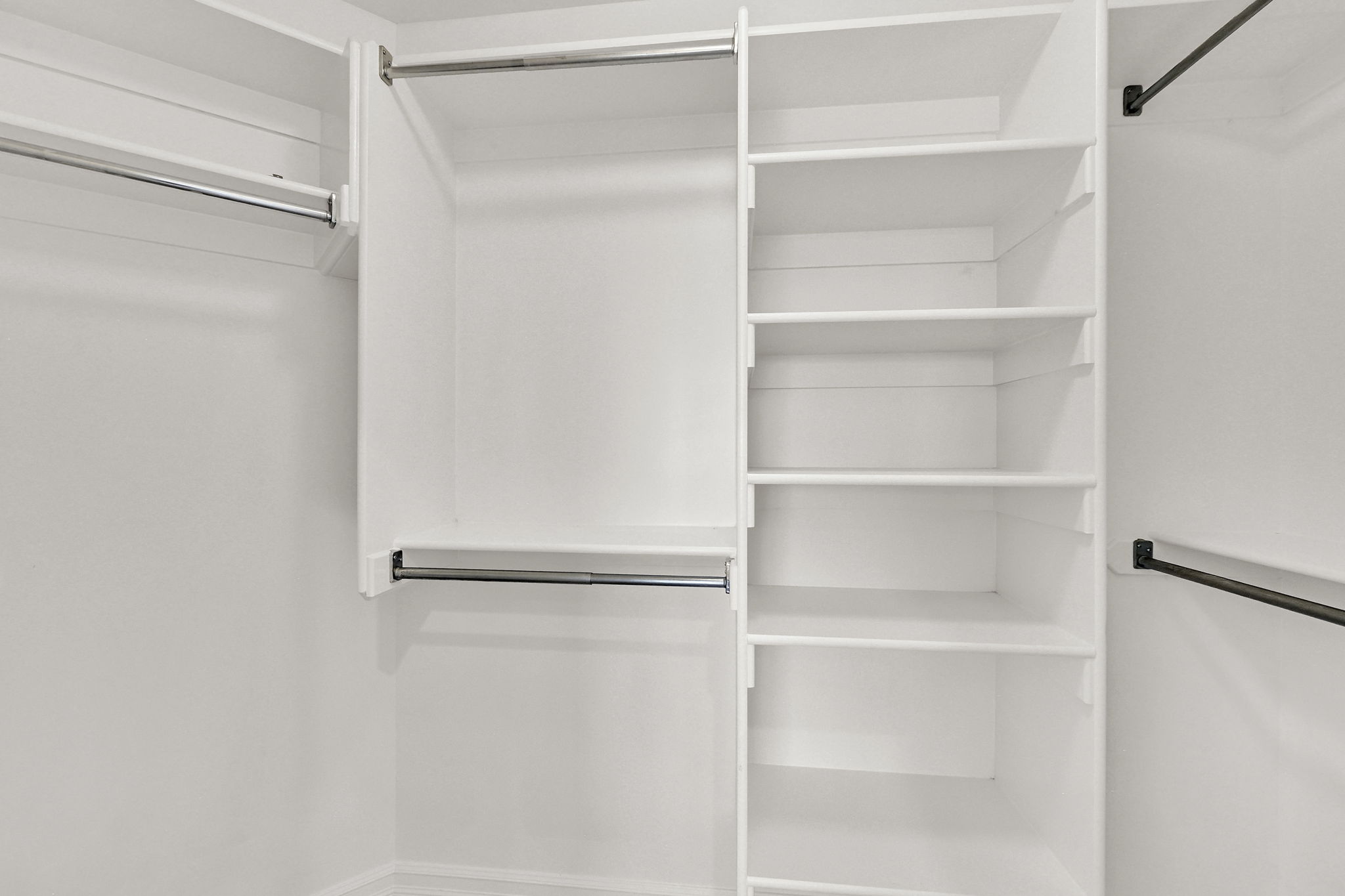 Built-in closet system featuring white shelving, multiple hanging rods, and integrated storage solutions