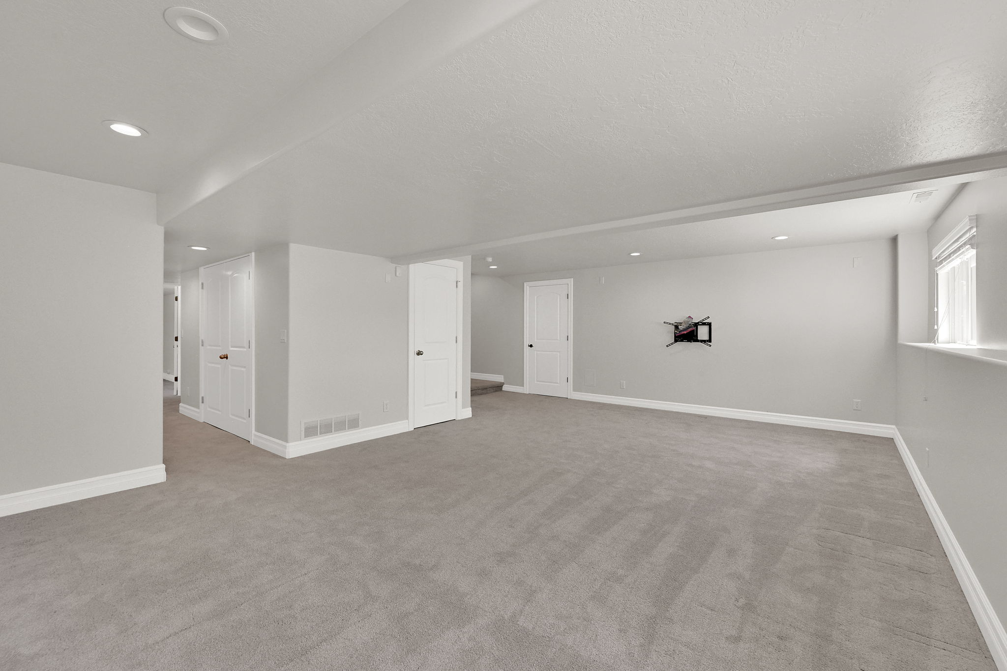 Spacious room featuring light gray carpeting, recessed lighting, white baseboards, and white interior doors