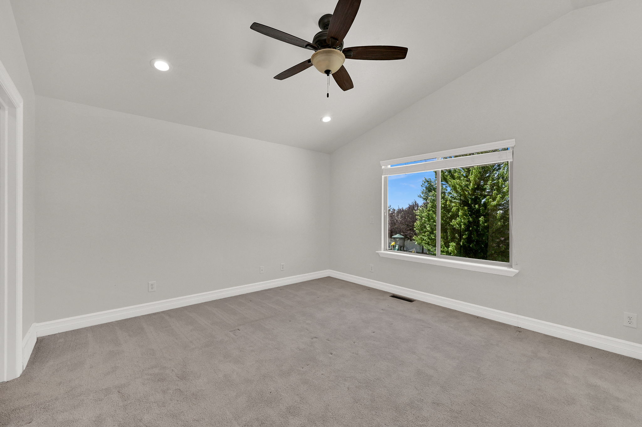 Vaulted ceiling room featuring light gray carpeting, a ceiling fan with integrated lighting, recessed lighting, and a large window with white trim