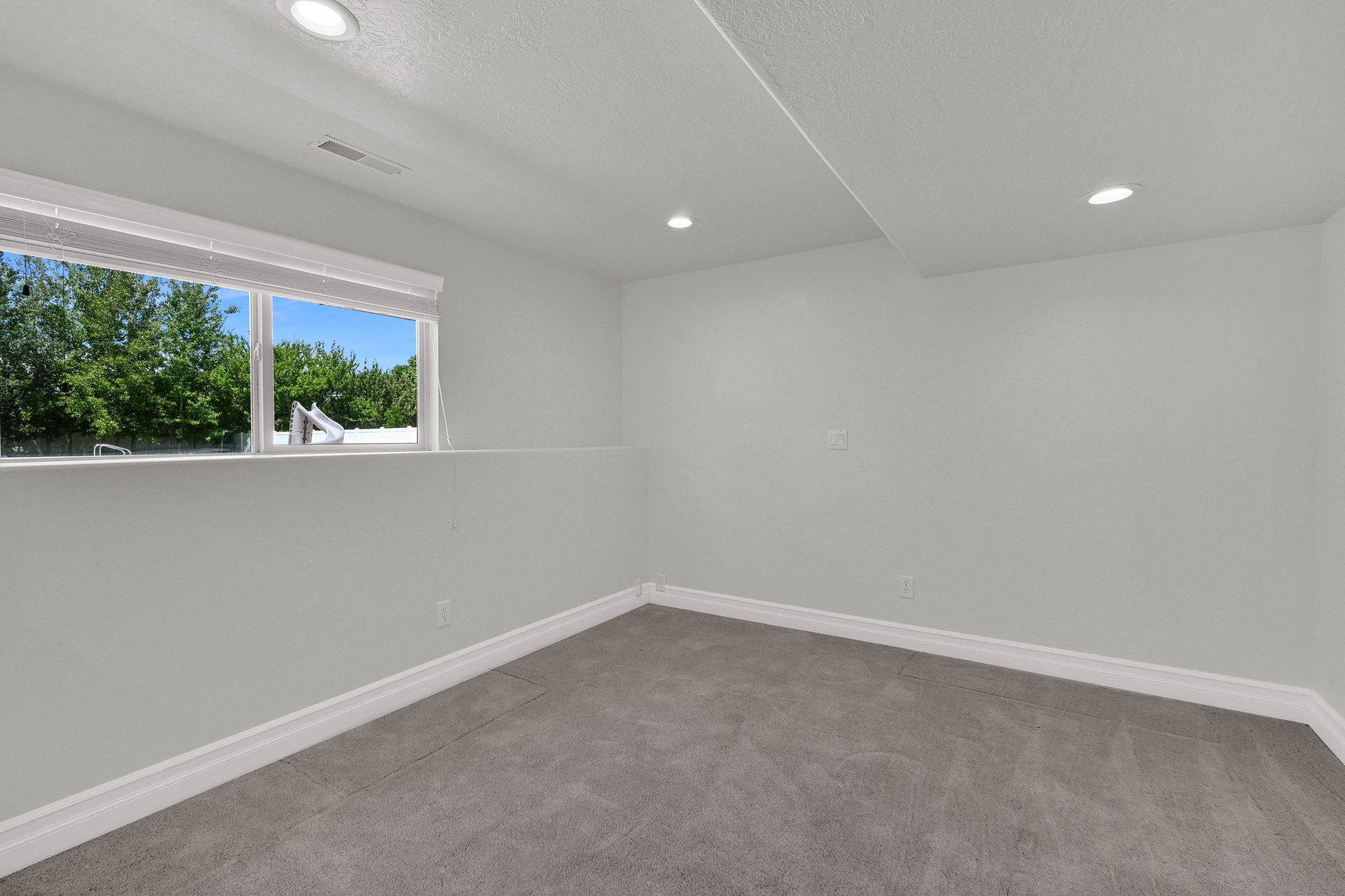 Carpeted bedroom with a large window, white trim, recessed lighting, and light gray walls