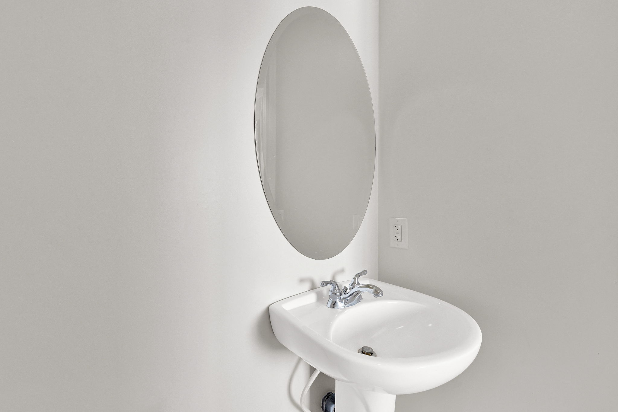 Pedestal sink with chrome faucet, complemented by an oval wall-mounted mirror