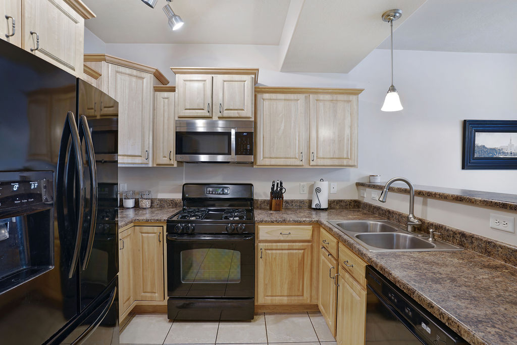 Kitchen featuring light wood cabinetry, stone-finish countertops, and a full suite of black and stainless steel appliances