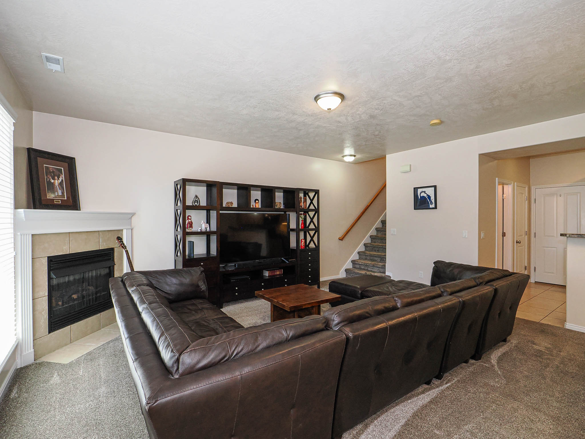 Living area featuring a tiled fireplace with a white mantel, light-toned walls, and grey carpet flooring