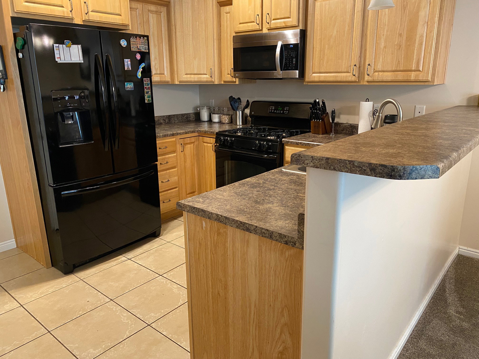 Kitchen featuring light wood cabinetry, stone-look laminate countertops, and tile flooring