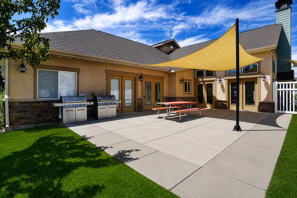 Expansive concrete patio with a shade sail, bordered by manicured turf