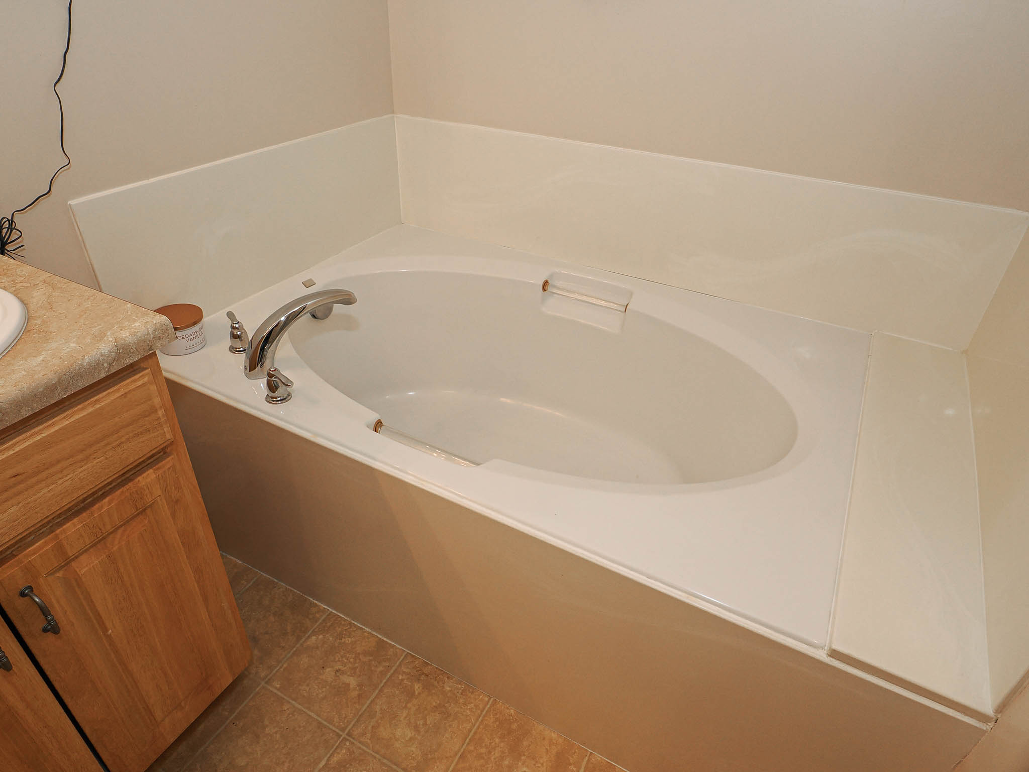 Built-in oval bathtub with deck-mounted chrome fixtures, surrounded by a light-toned enclosure