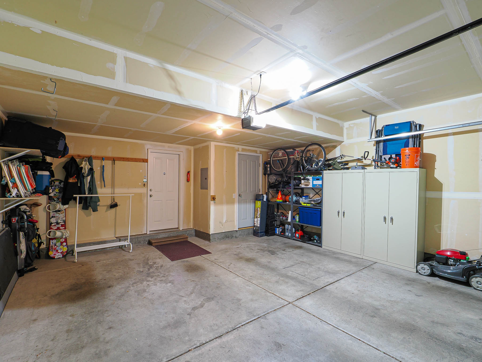 Spacious garage featuring a concrete floor, exposed ceiling joists, and multiple storage solutions