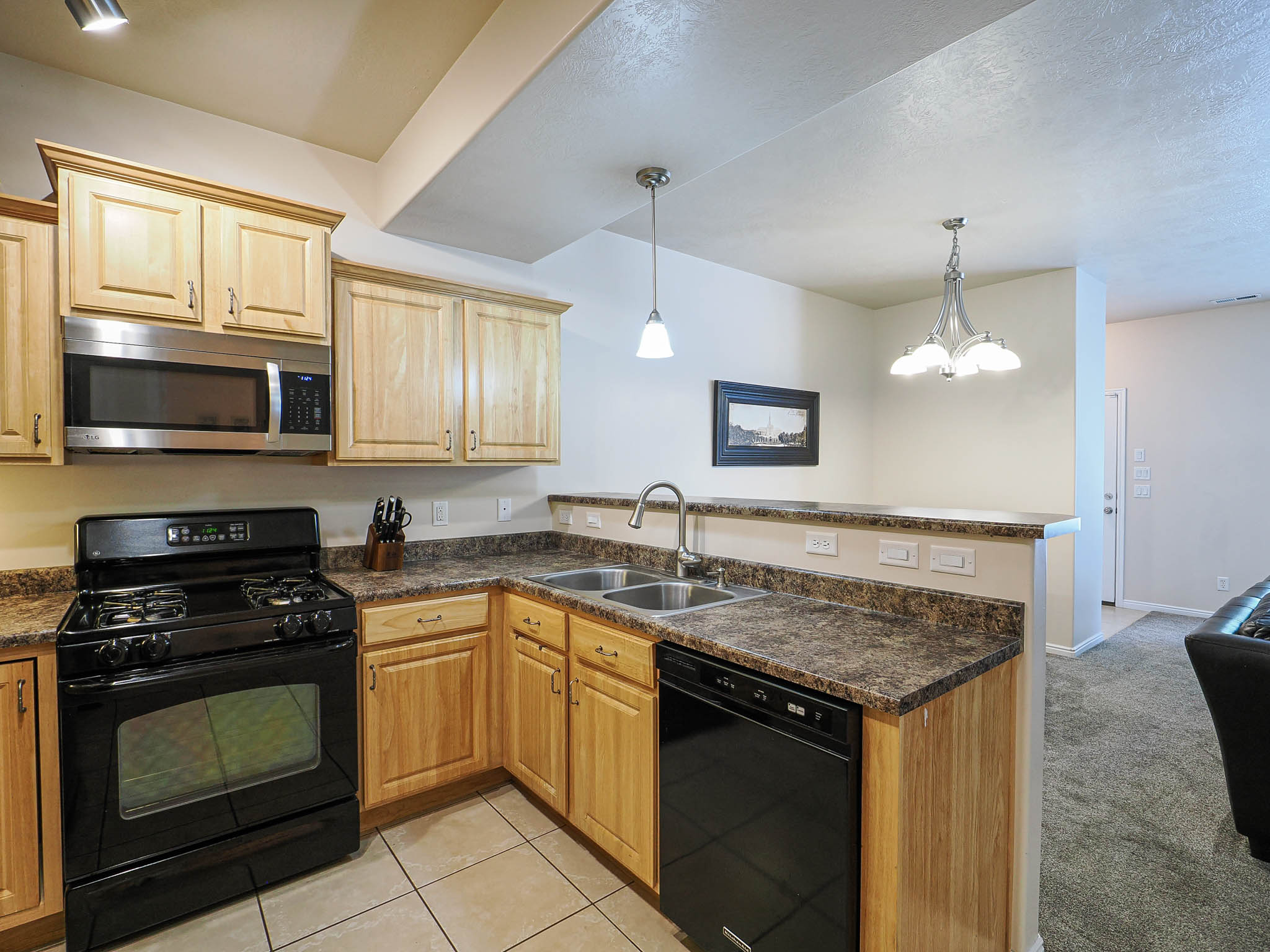 Kitchen featuring light wood cabinetry, stone-look countertops, and stainless steel appliances including a microwave and dishwasher