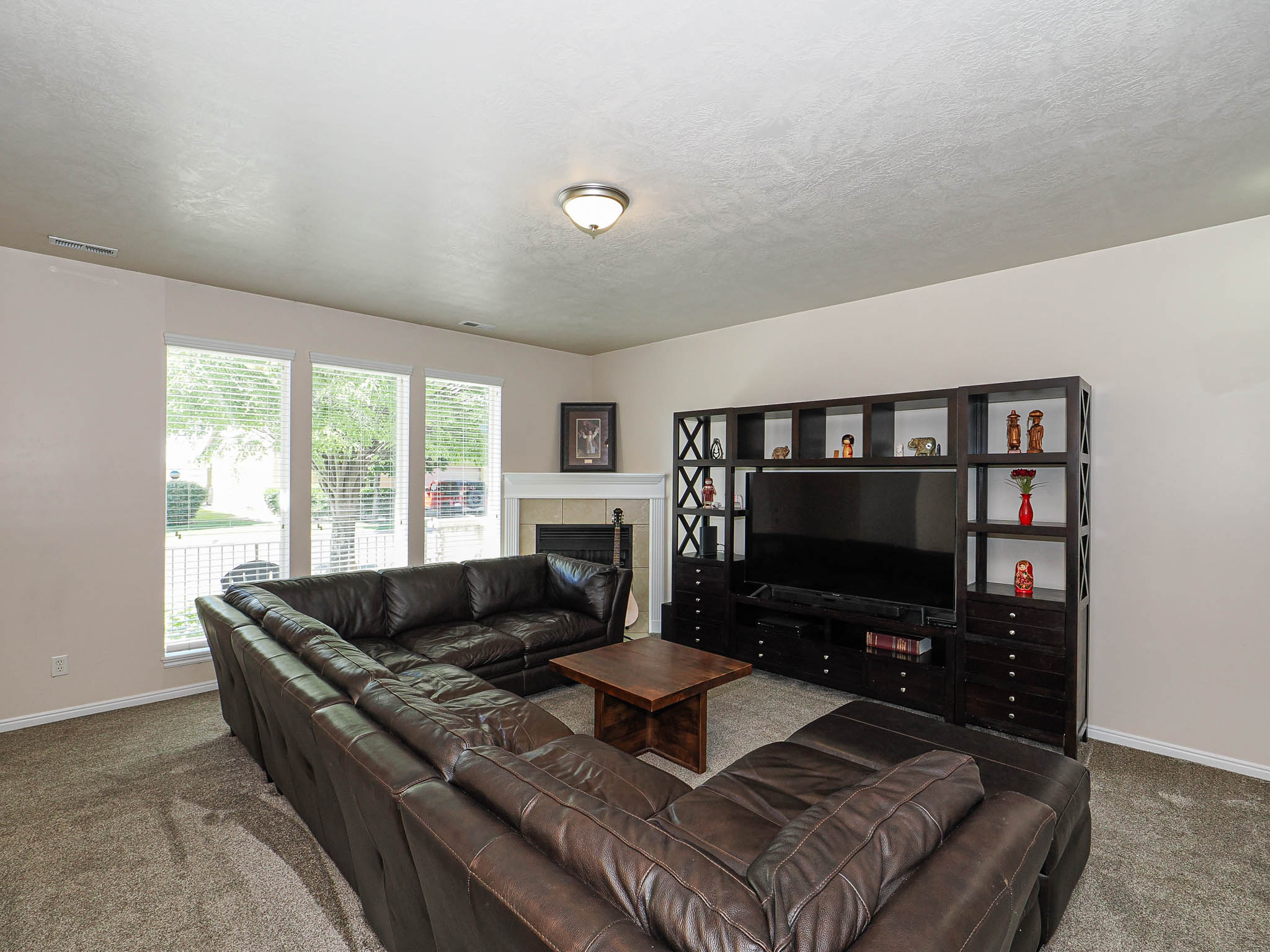 Carpeted living area featuring multiple windows with blinds, a built-in entertainment center, a fireplace with a mantel, and light-toned wall finishes