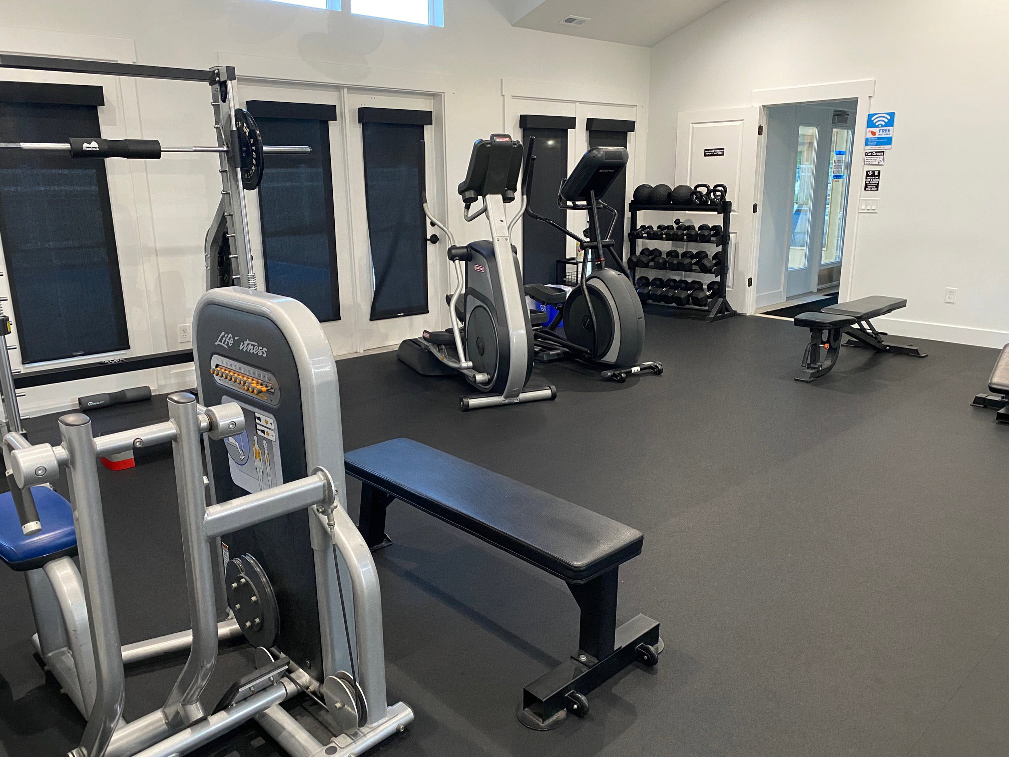 Dedicated fitness area featuring black rubber flooring, tall ceilings, and ample natural light from high windows