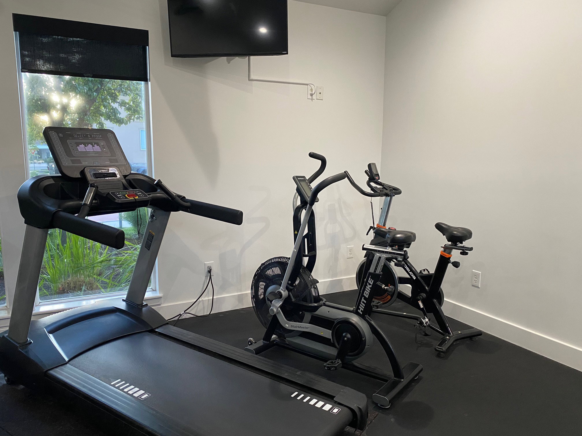 Dedicated fitness area featuring durable black rubber flooring and a window with a roller shade